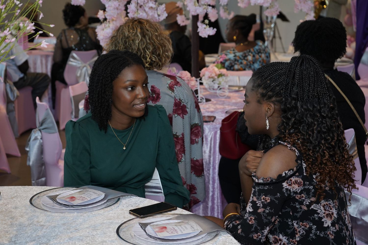 A group of people gathered around tables at a celebratory event with pink decor.