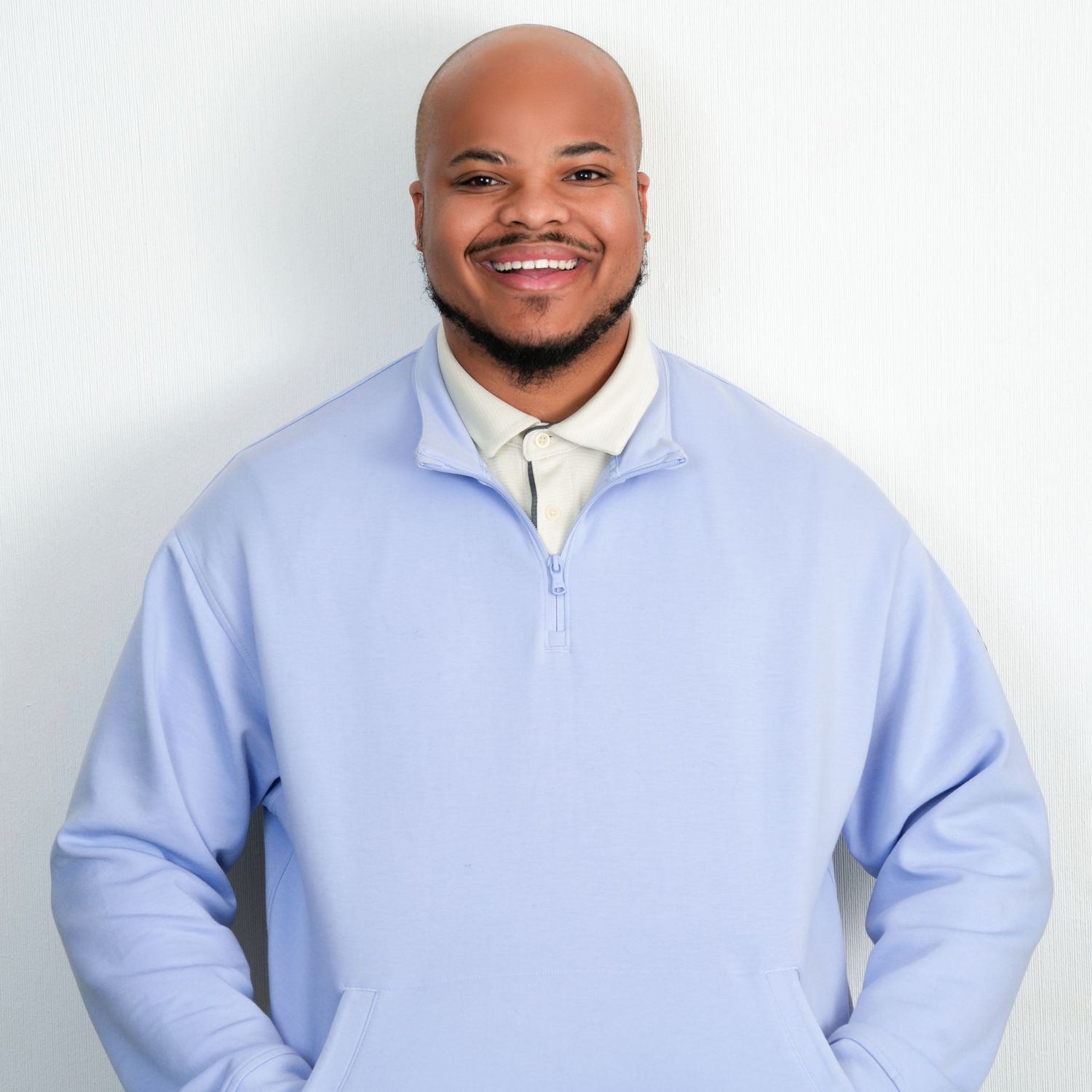 Professional wearing a light blue button-down shirt poses against white background in studio setting.