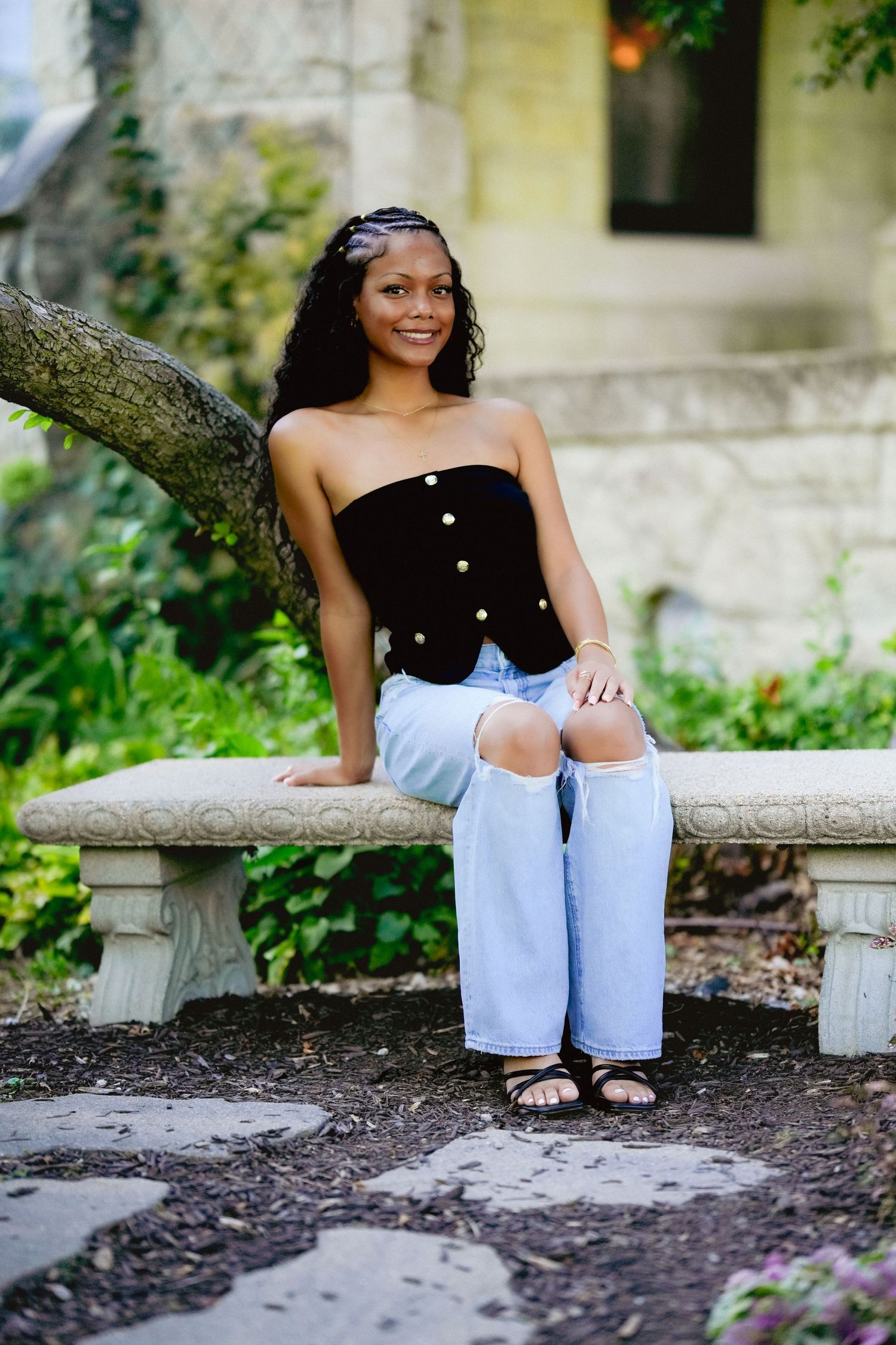 Outdoor photoshoot on stone steps surrounded by greenery wearing casual denim and black top.
