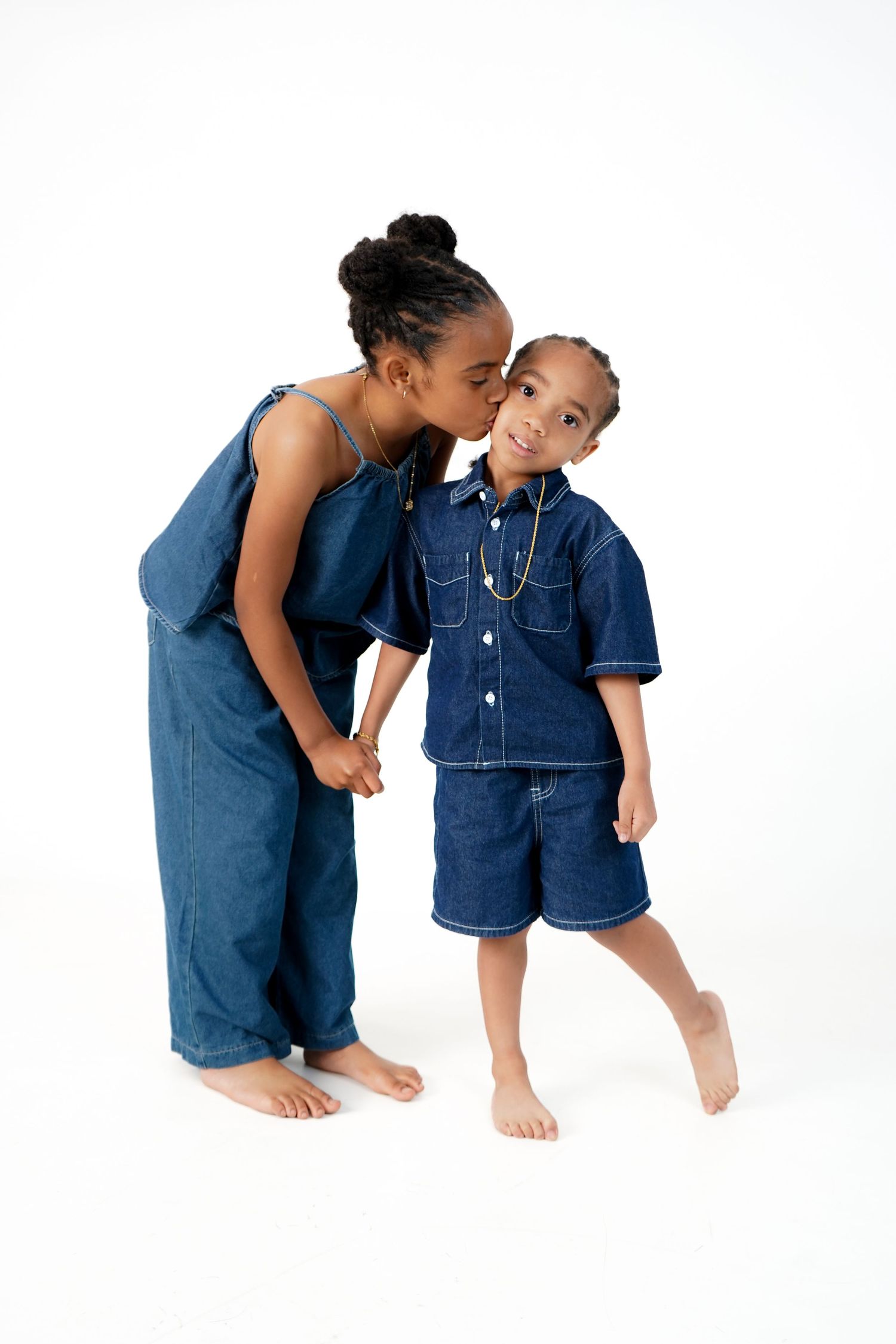Two children in matching denim outfits lean towards each other playfully in a sequence of three poses against a white backdrop.