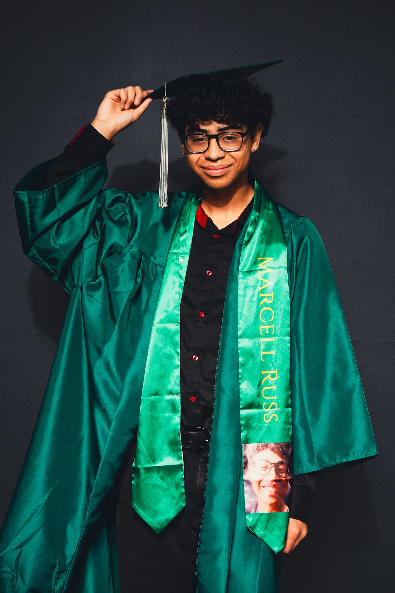 Graduate wearing emerald green cap and gown with decorative sash poses for photos.