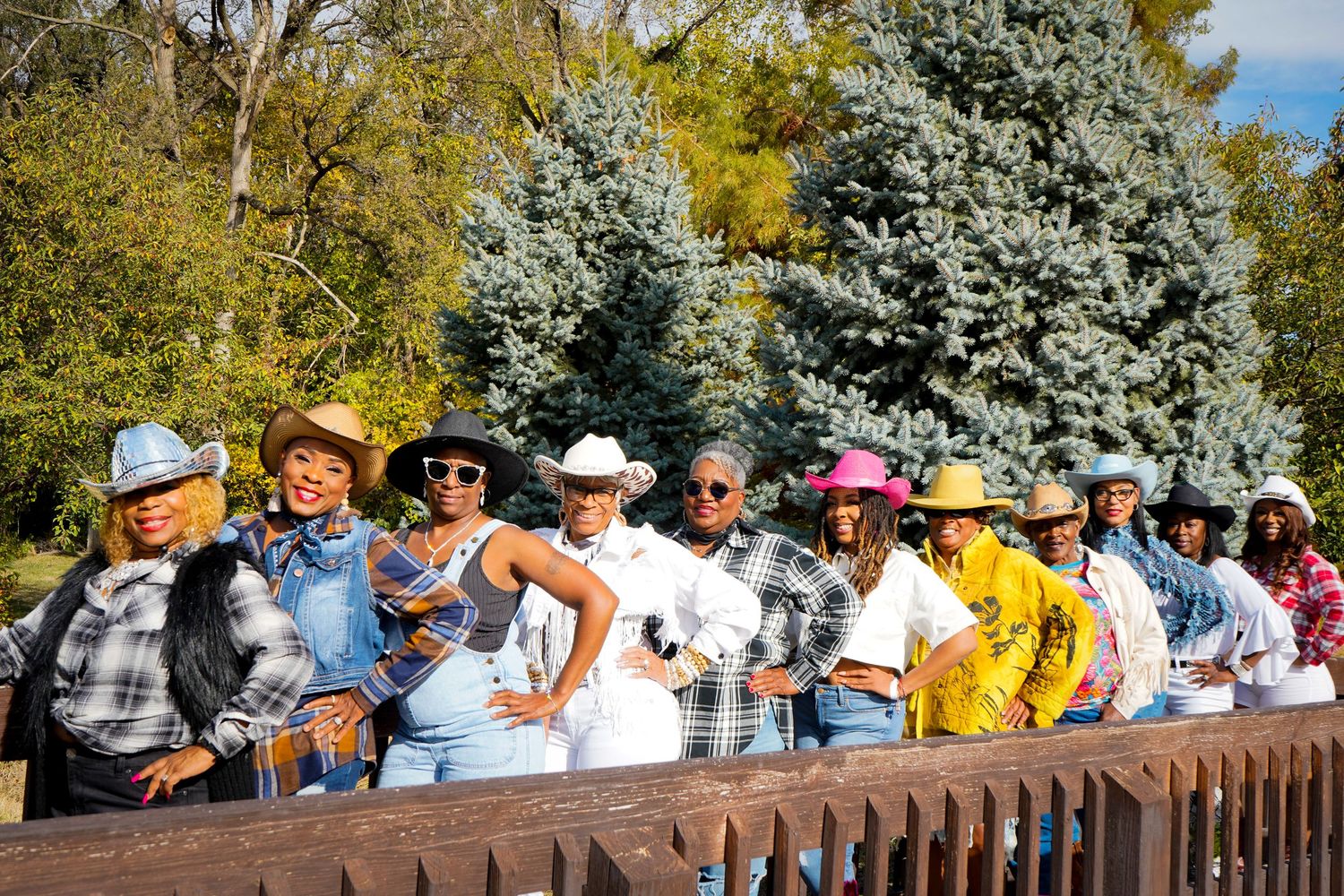 A crowd of spectators leans against a wooden railing while watching an event outdoors on a sunny day.