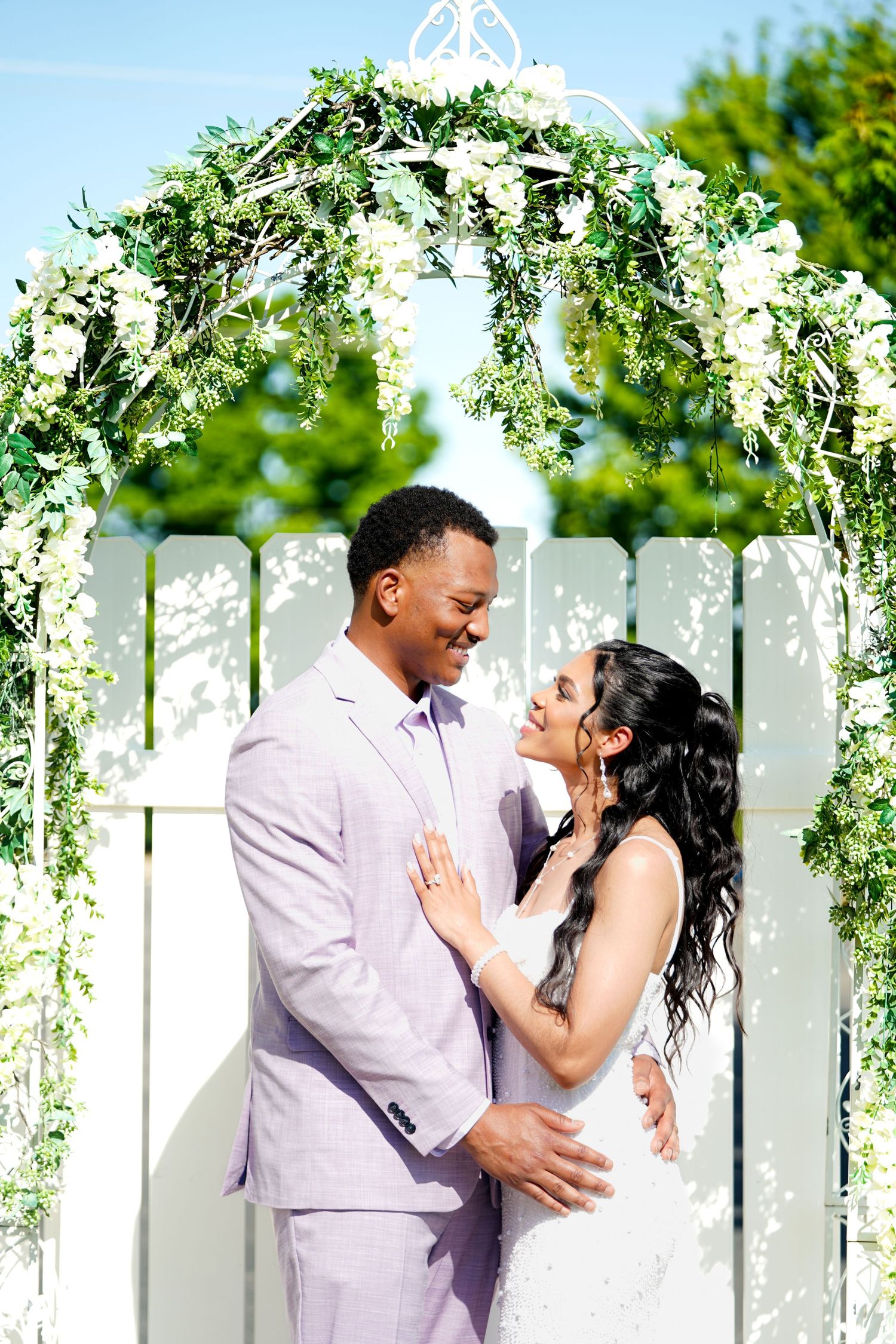 A romantic moment captured in a series of photos under a white floral arch in an outdoor garden setting.