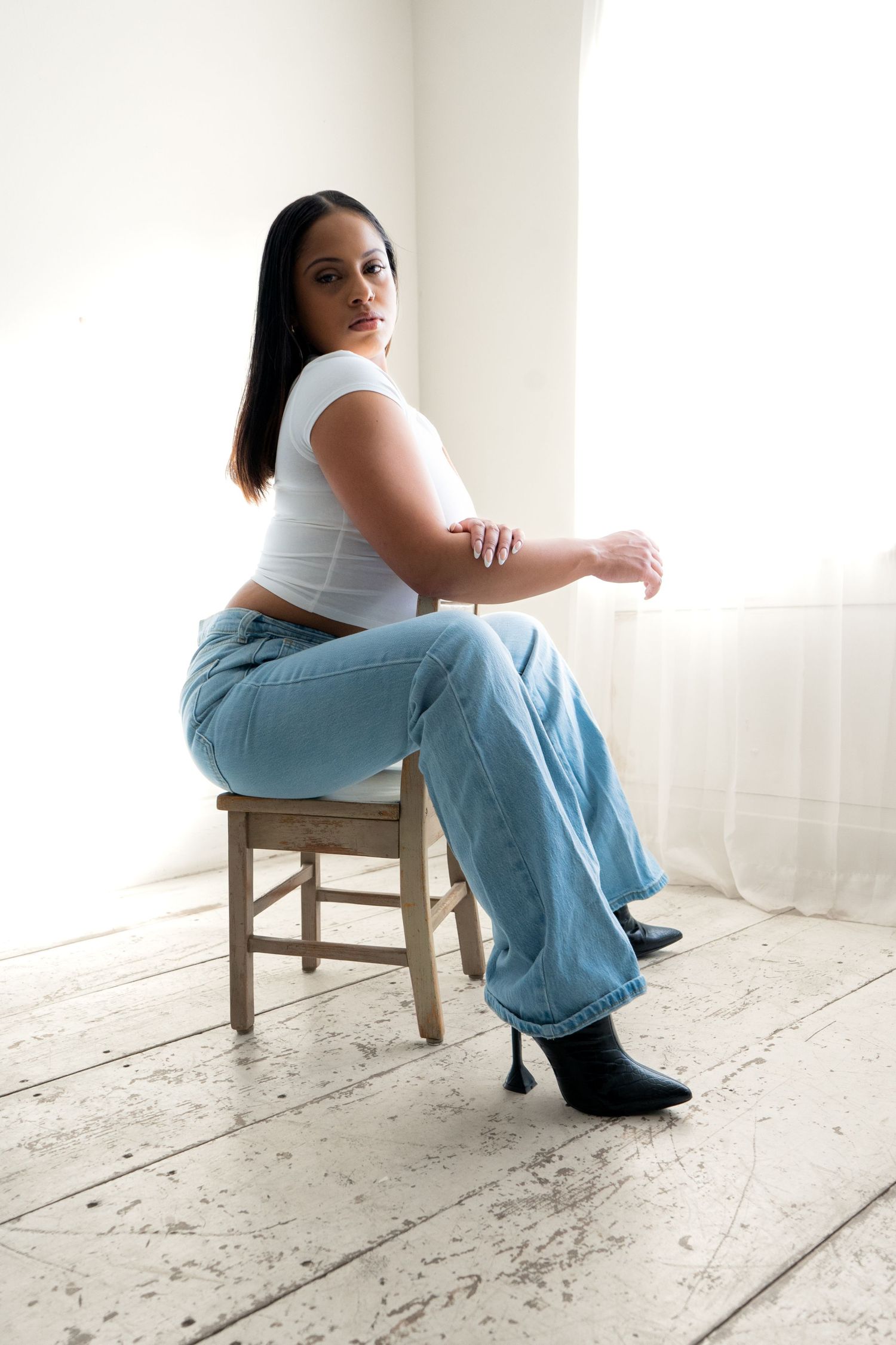 Minimalist portrait series on wooden chair against white floor and wall wearing casual denim.