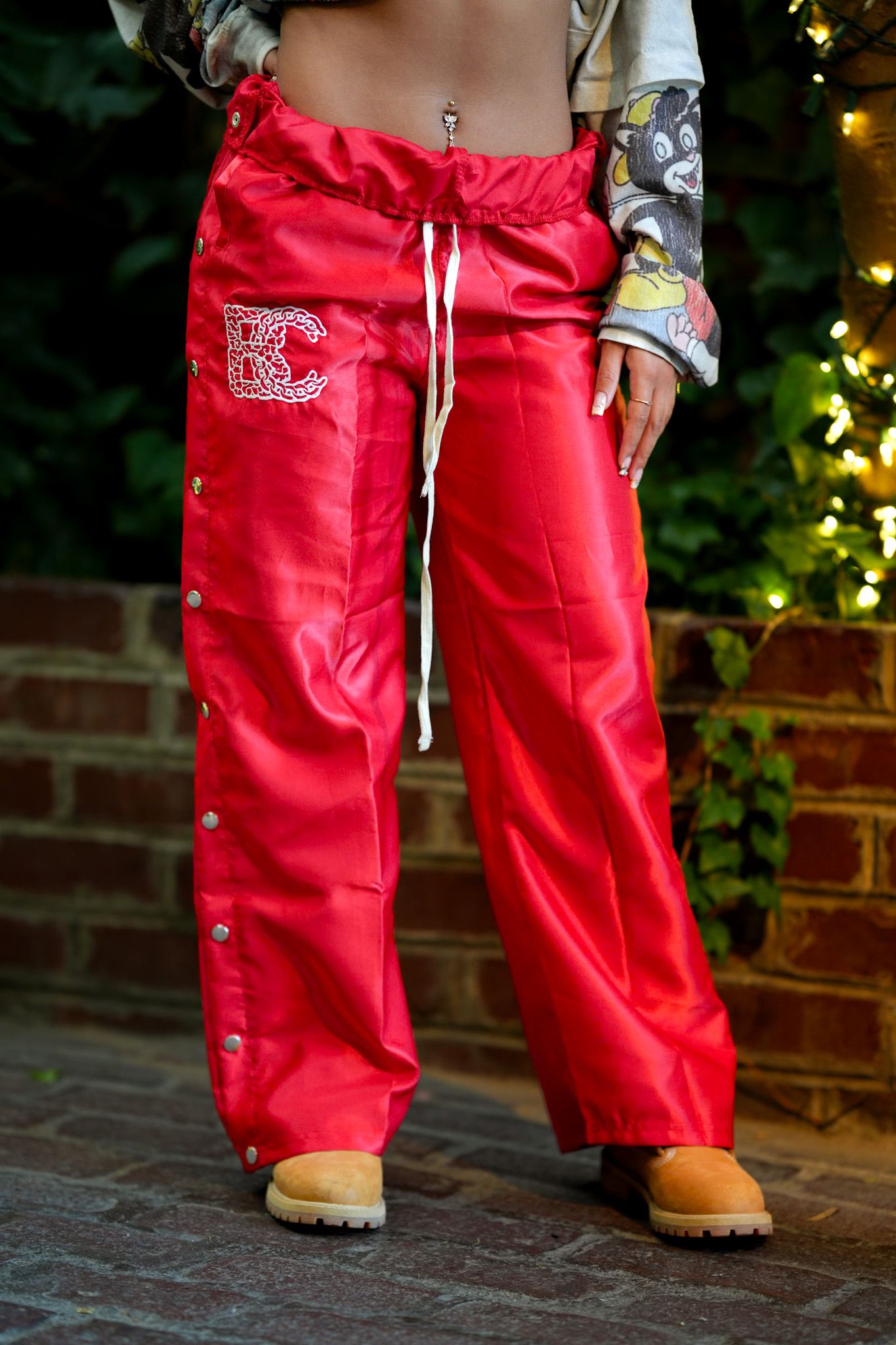 Red athletic pants with drawstring waist shown in detail against brick wall.