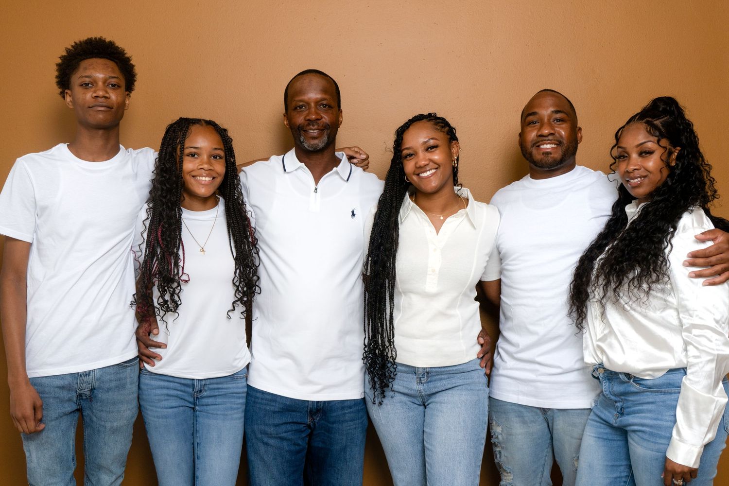 A group wearing matching white tops and blue jeans poses together in a casual indoor setting.