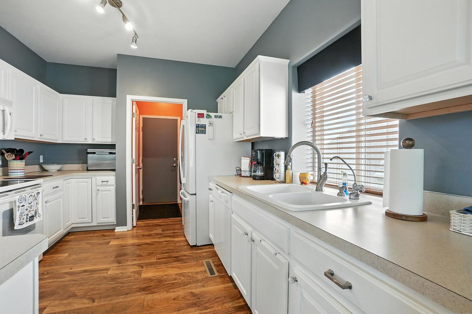 Modern kitchen with white cabinets, wood flooring, and stainless steel appliances features a long galley-style layout.