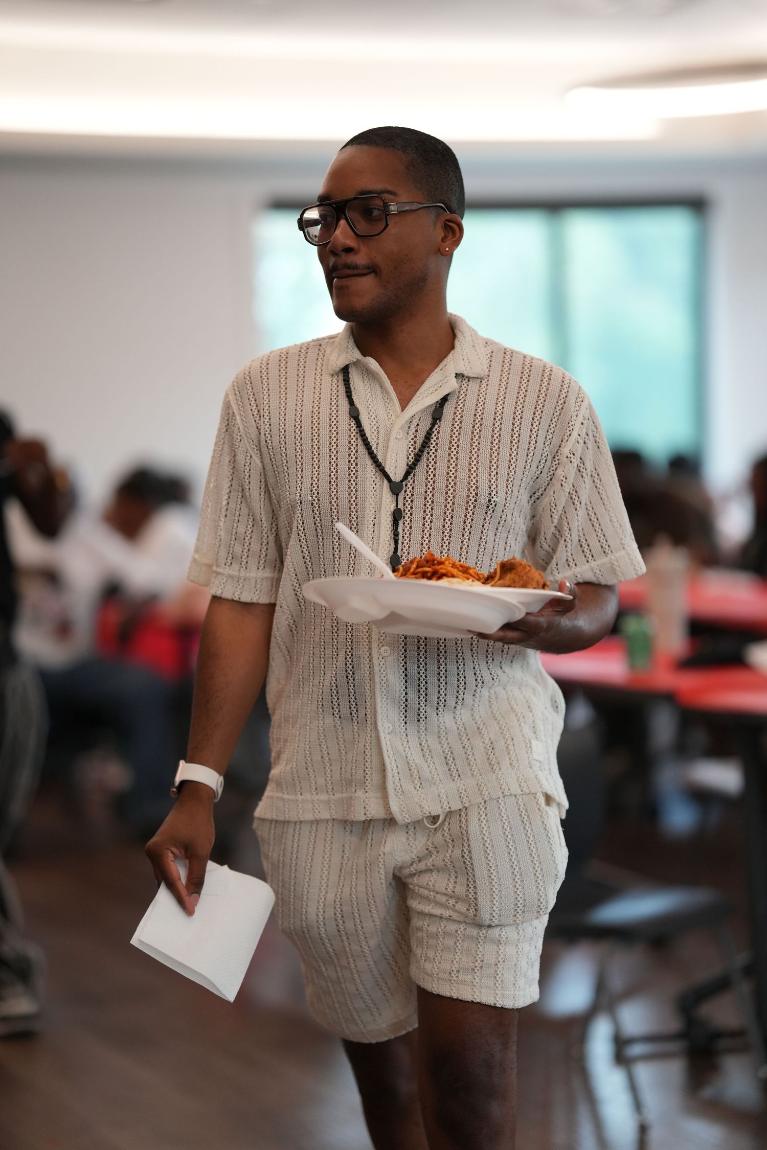 Person in a striped white shirt carries plates of food in a cafeteria setting.