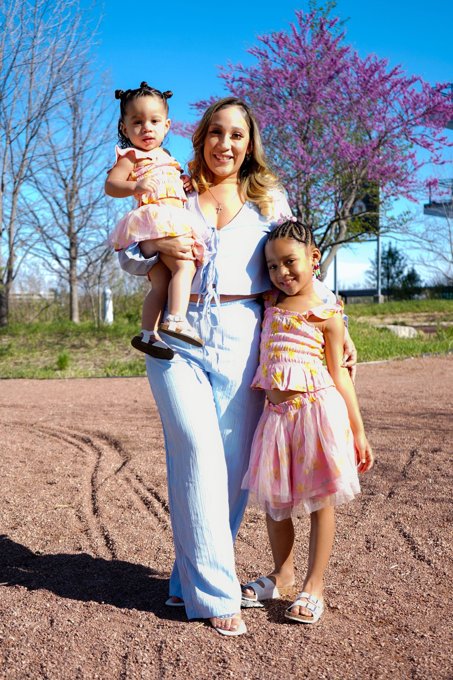 Three outdoor photos of children in spring outfits playing together on brown dirt ground with flowering trees in background.