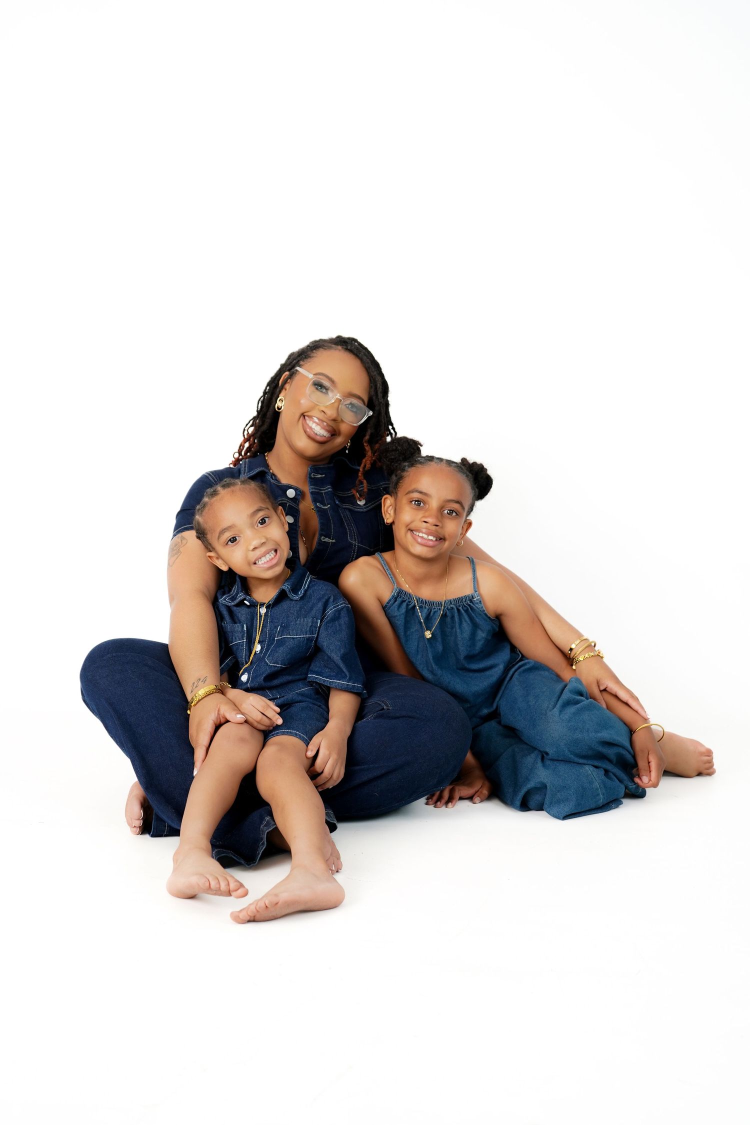 Four children in matching navy blue outfits lie playfully on the floor in a casual studio portrait setting.