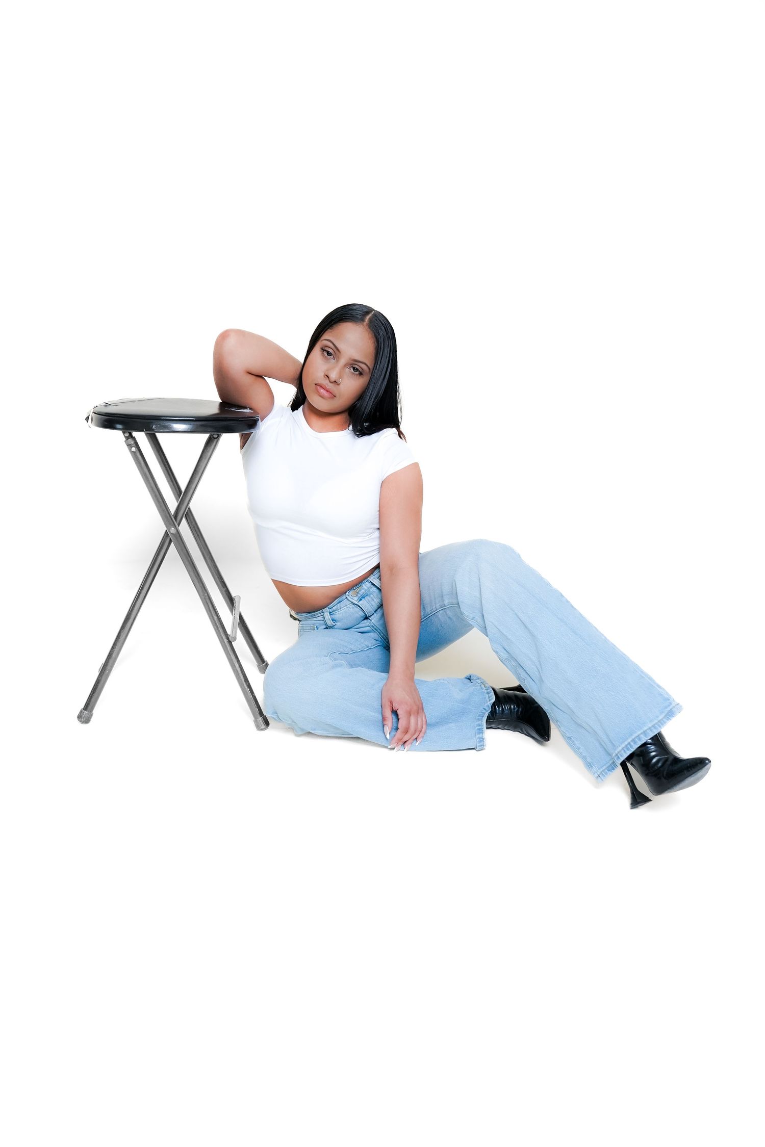 Casual lounging poses on a metal folding table wearing light denim and white top.