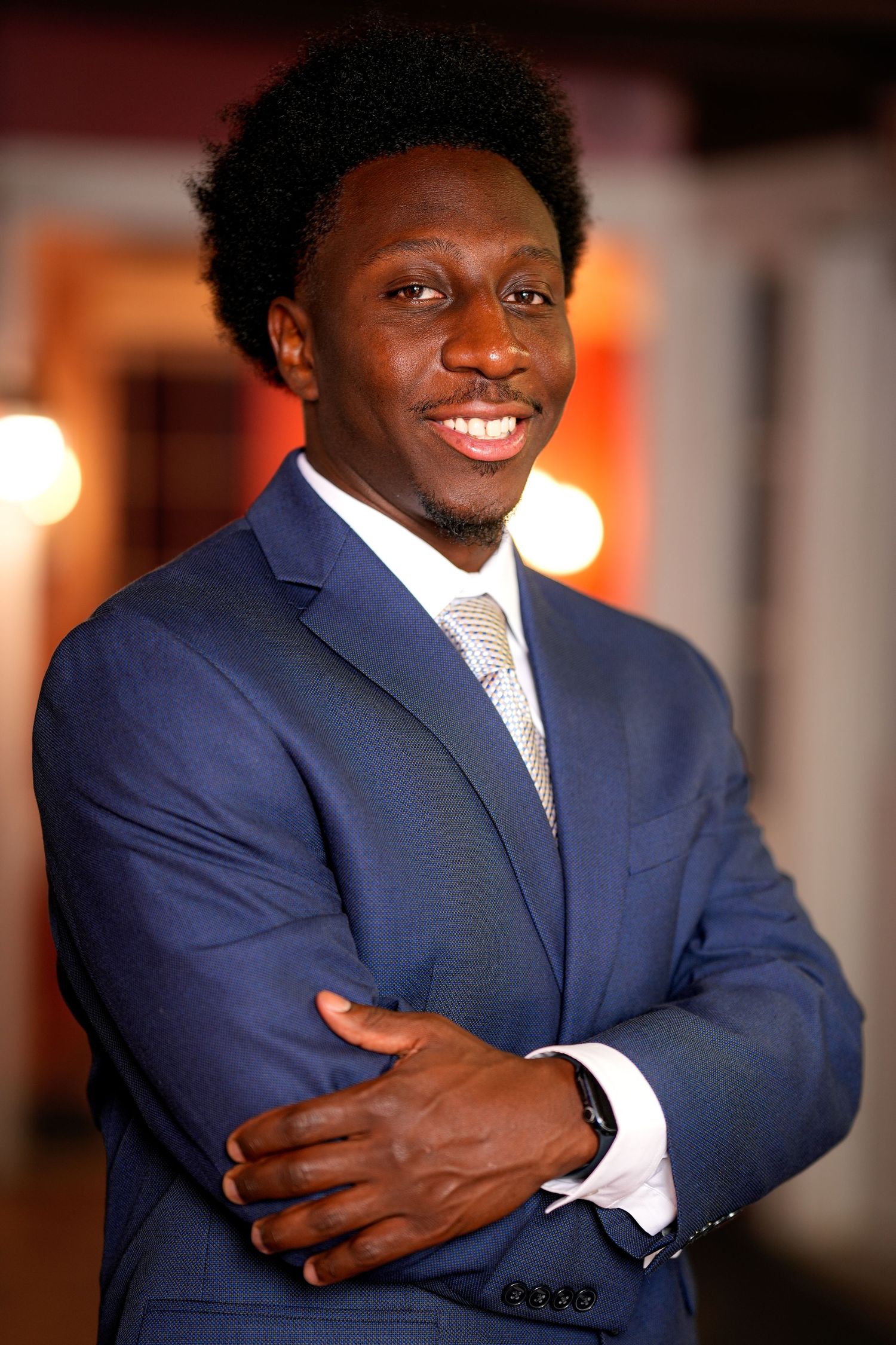 Professional portrait series showing someone in a navy blue suit and white shirt with crossed arms and warm lighting.