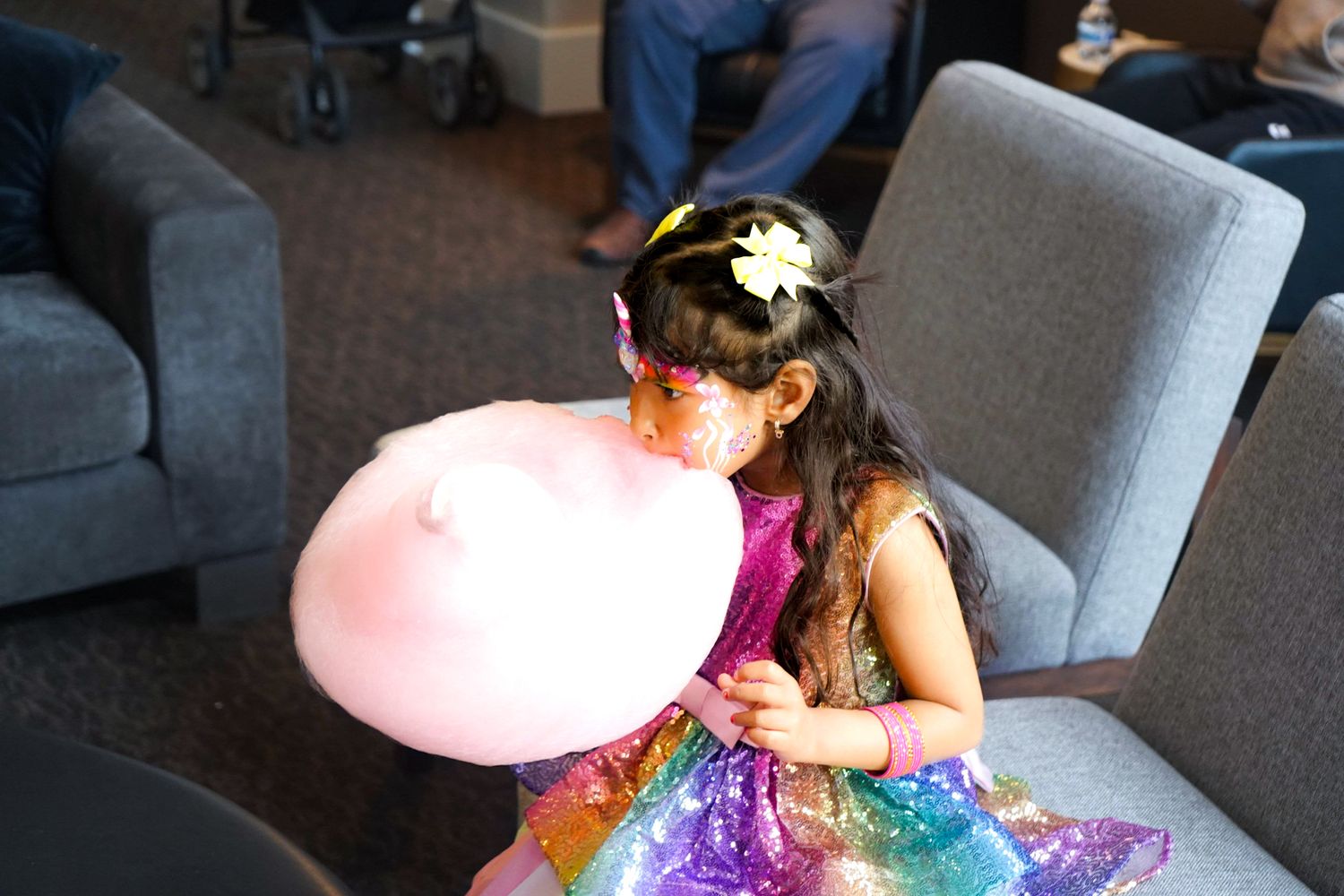 A person in a colorful dress holds a large pink cotton candy at an indoor event.