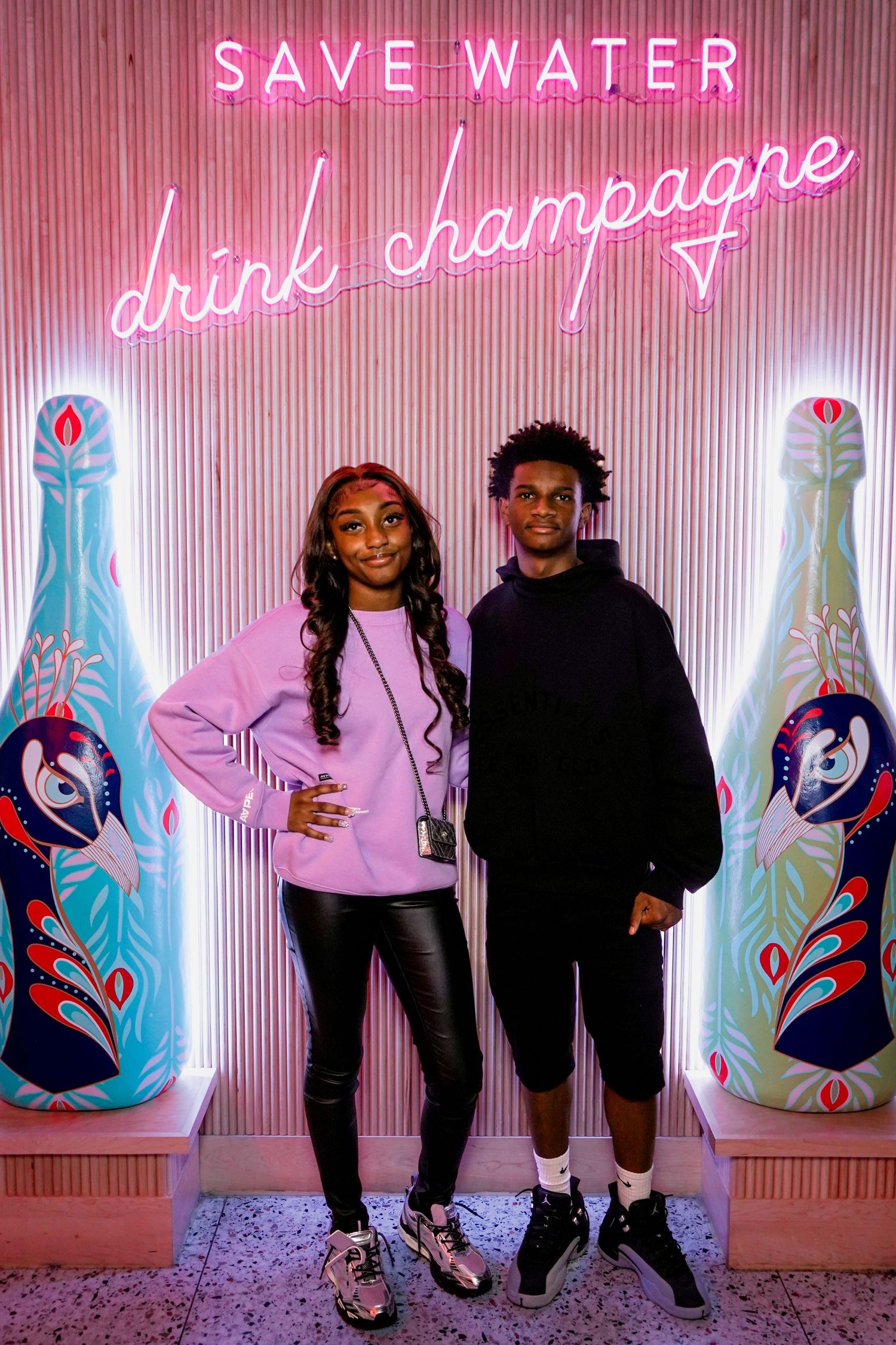 A series of illuminated neon signs on a pink wall displaying 'Save Water' and beverage-related text in glowing letters.