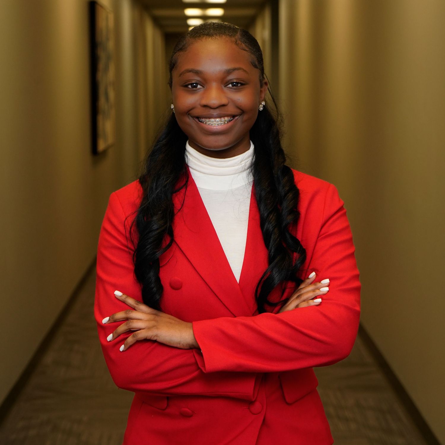 Professional headshot of person in black suit with red tie and long braided hair.