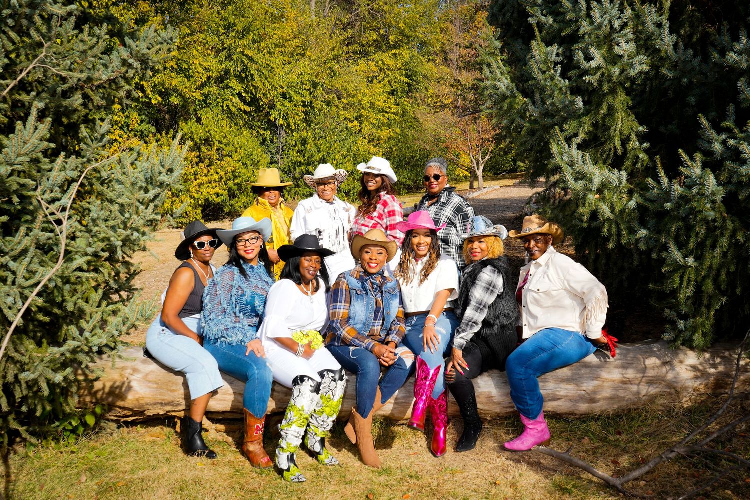 A cheerful group sits together on a stone wall surrounded by autumn foliage in a sunny outdoor setting.