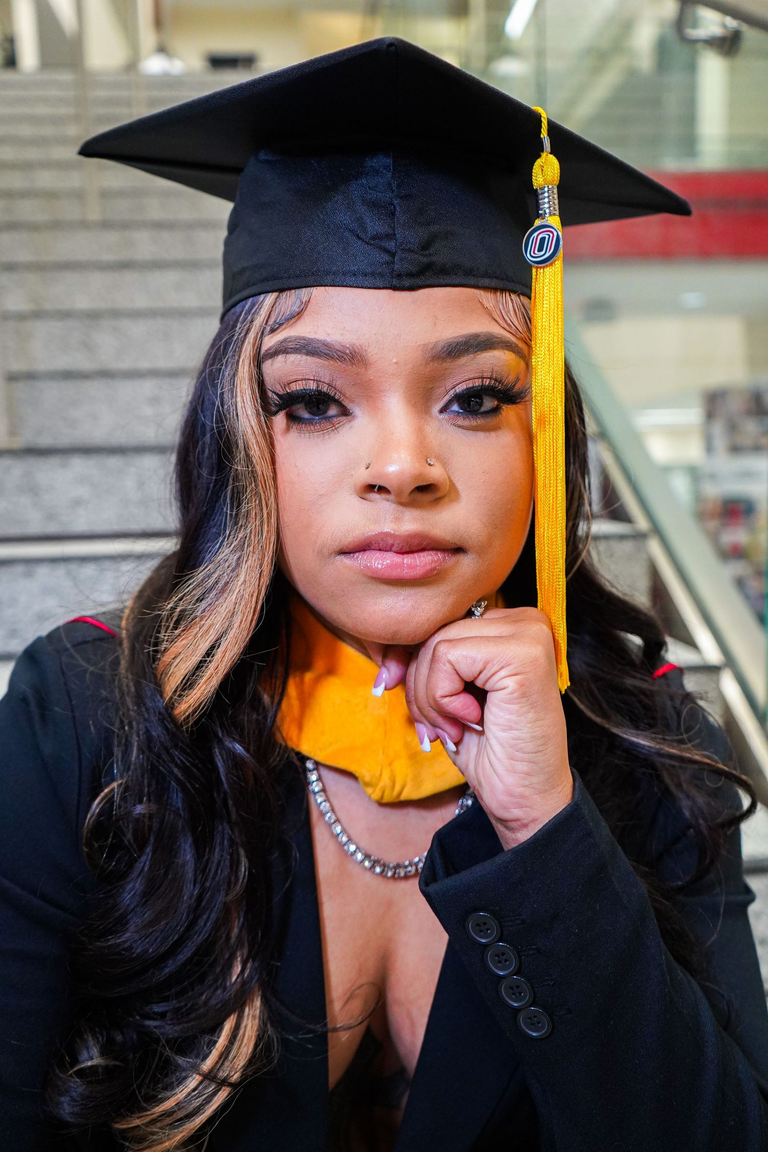 Graduate in black cap and gown with yellow tassel poses for professional photos.