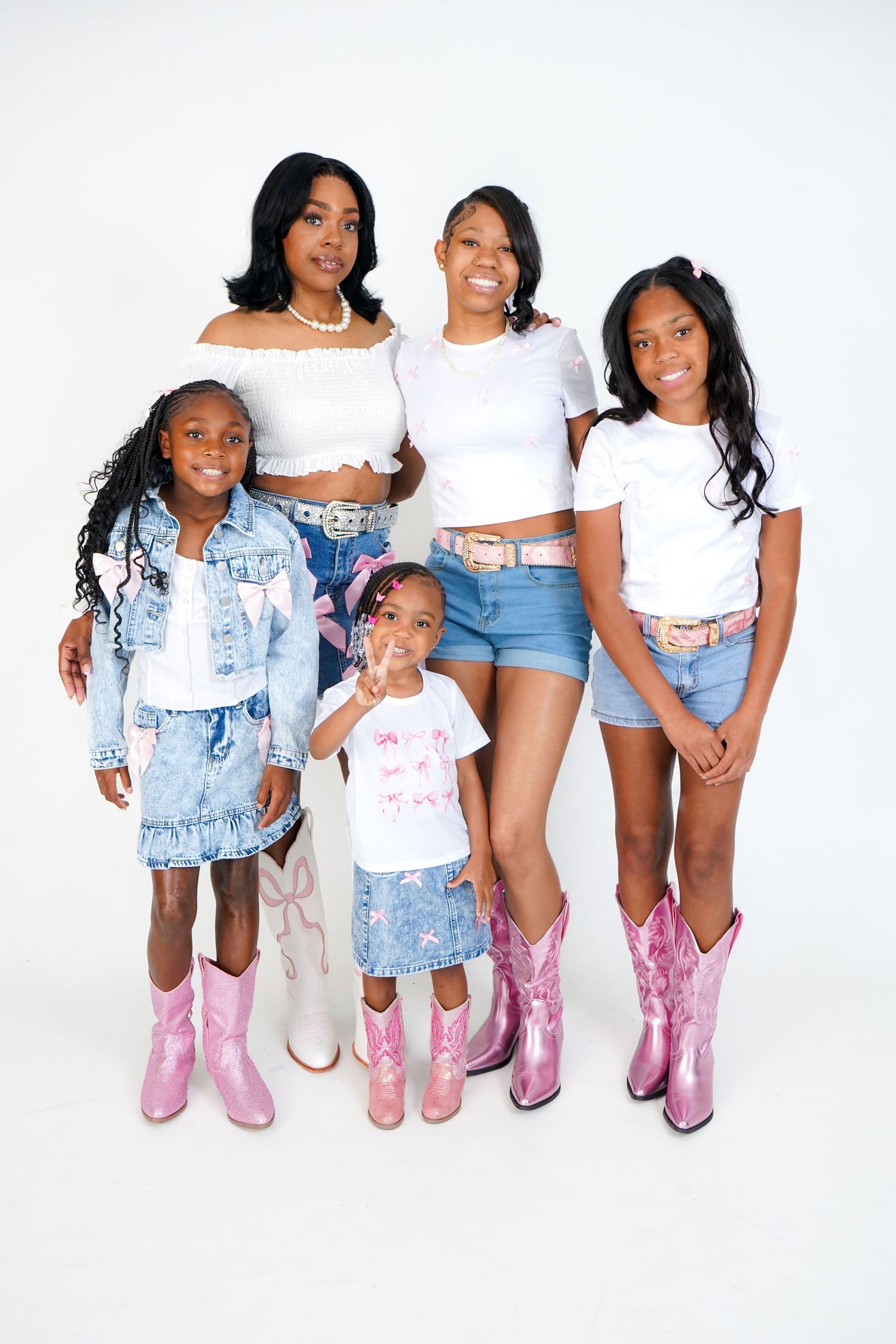 A group wearing matching pink cowboy boots pose together in casual denim and white outfits against a white backdrop.
