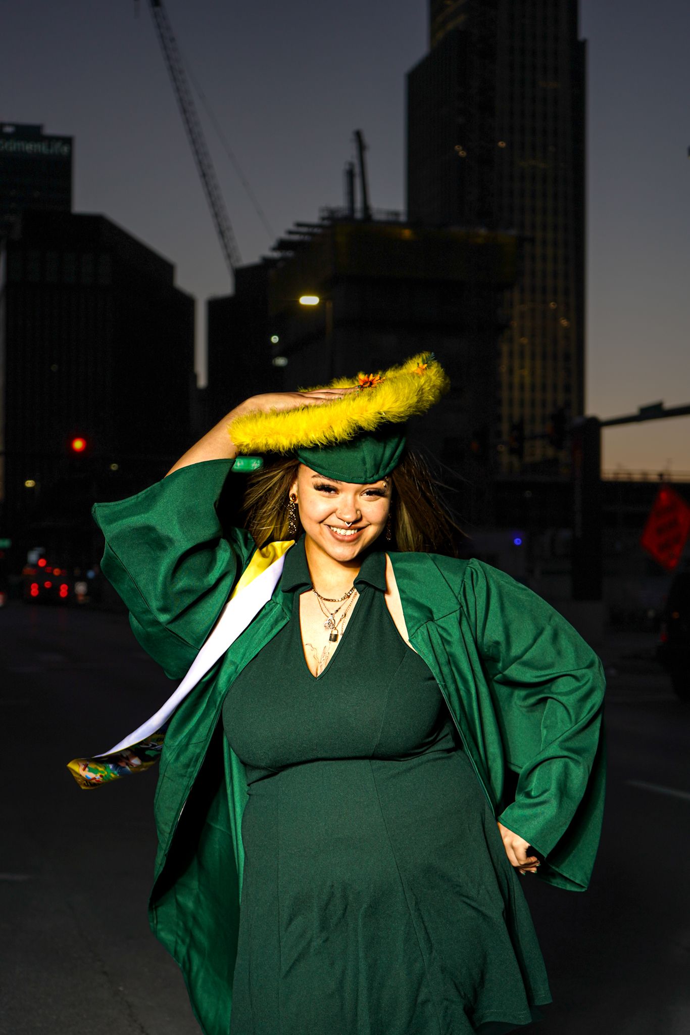 Nighttime graduation photos with green academic regalia against city skyline.
