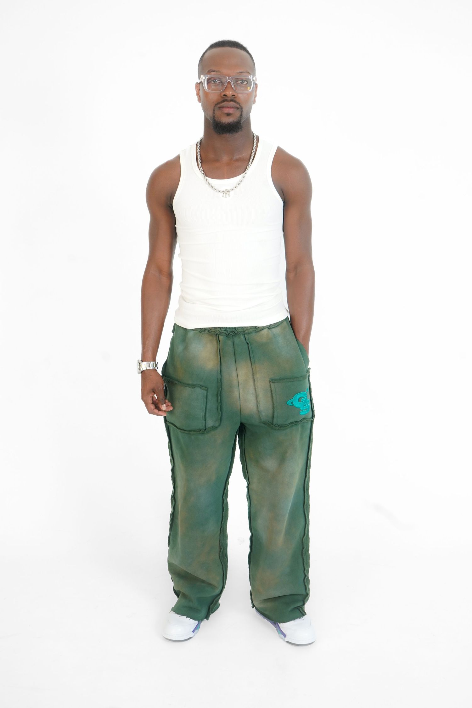Model showcases green cargo pants with white tank top in fashion product photography.