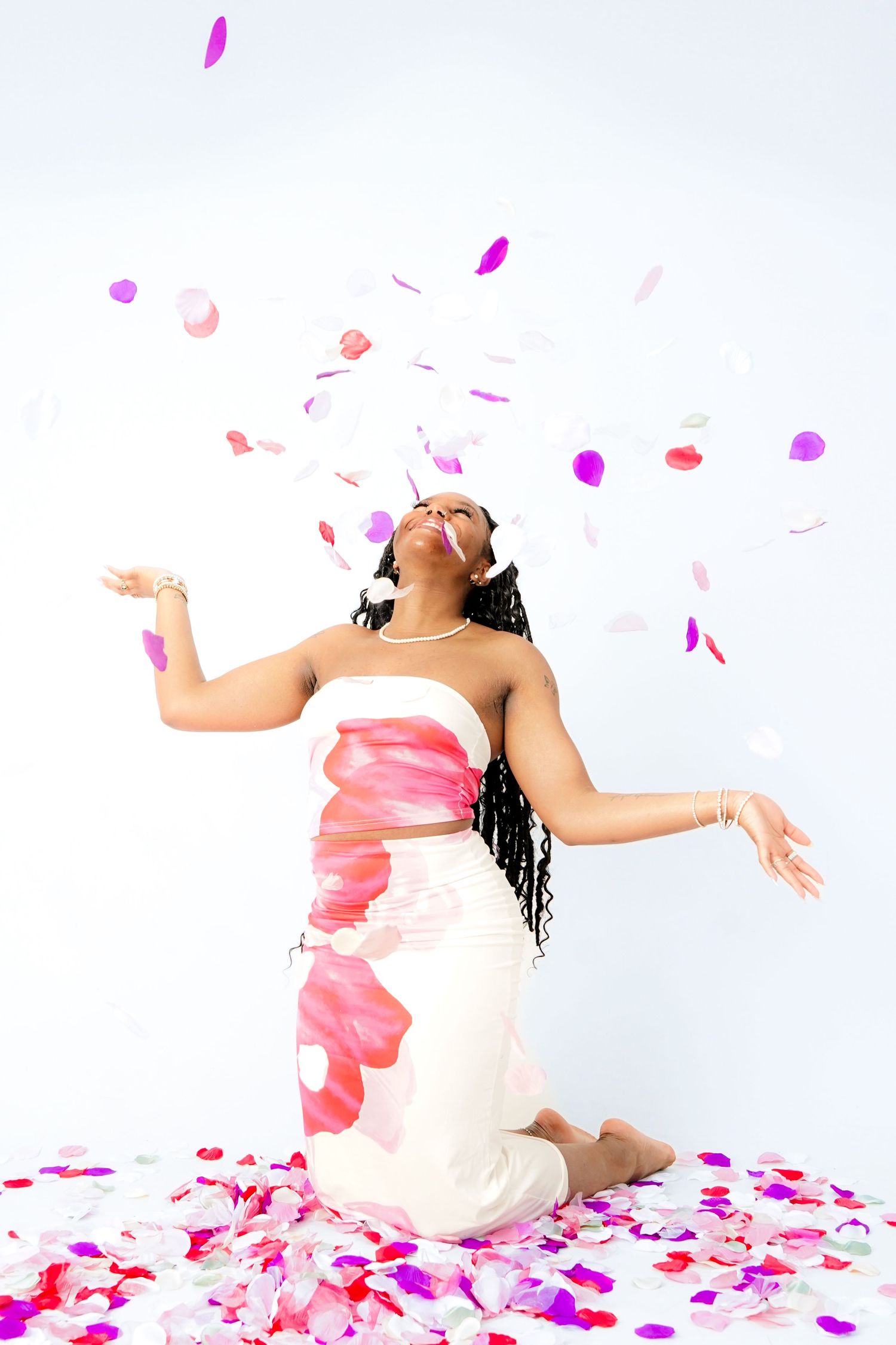 Artistic portrait with pink and white rose petals against white background in flowing dress.
