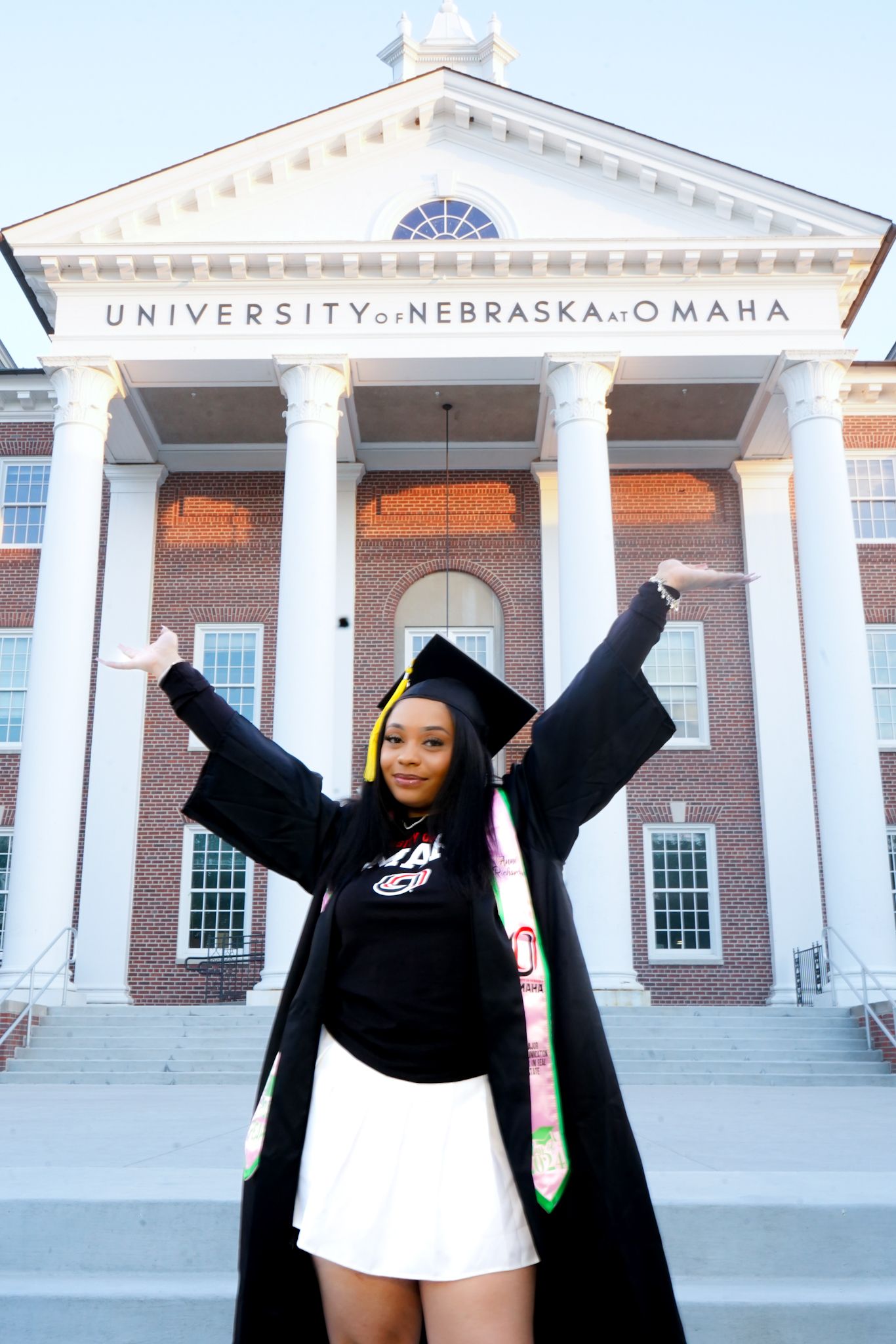 Celebratory graduation poses in front of University of Nebraska Omaha building entrance.