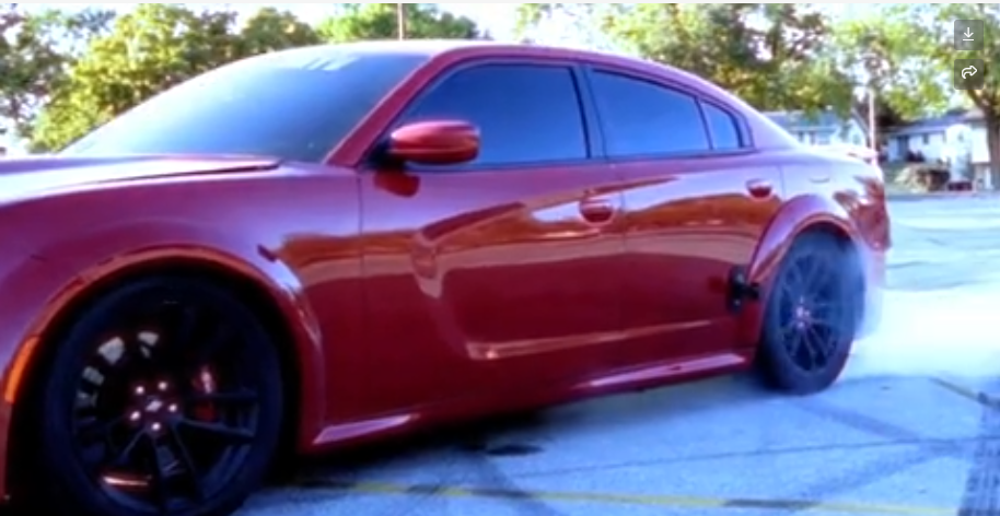 Red Dodge Charger with black wheels parked on a street in daylight.
