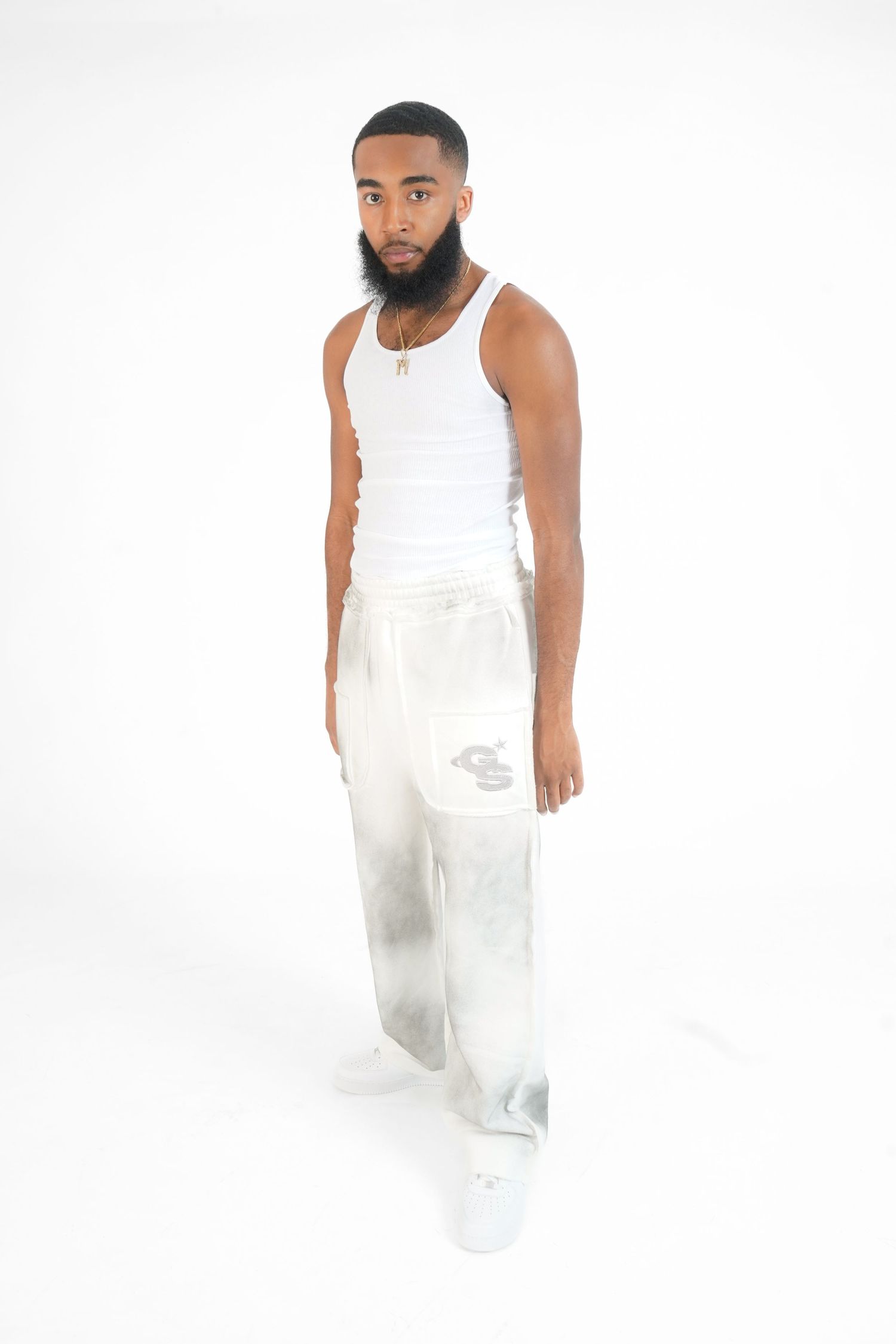 Man wearing white tank top and matching pants poses against white background in fashion lookbook series.