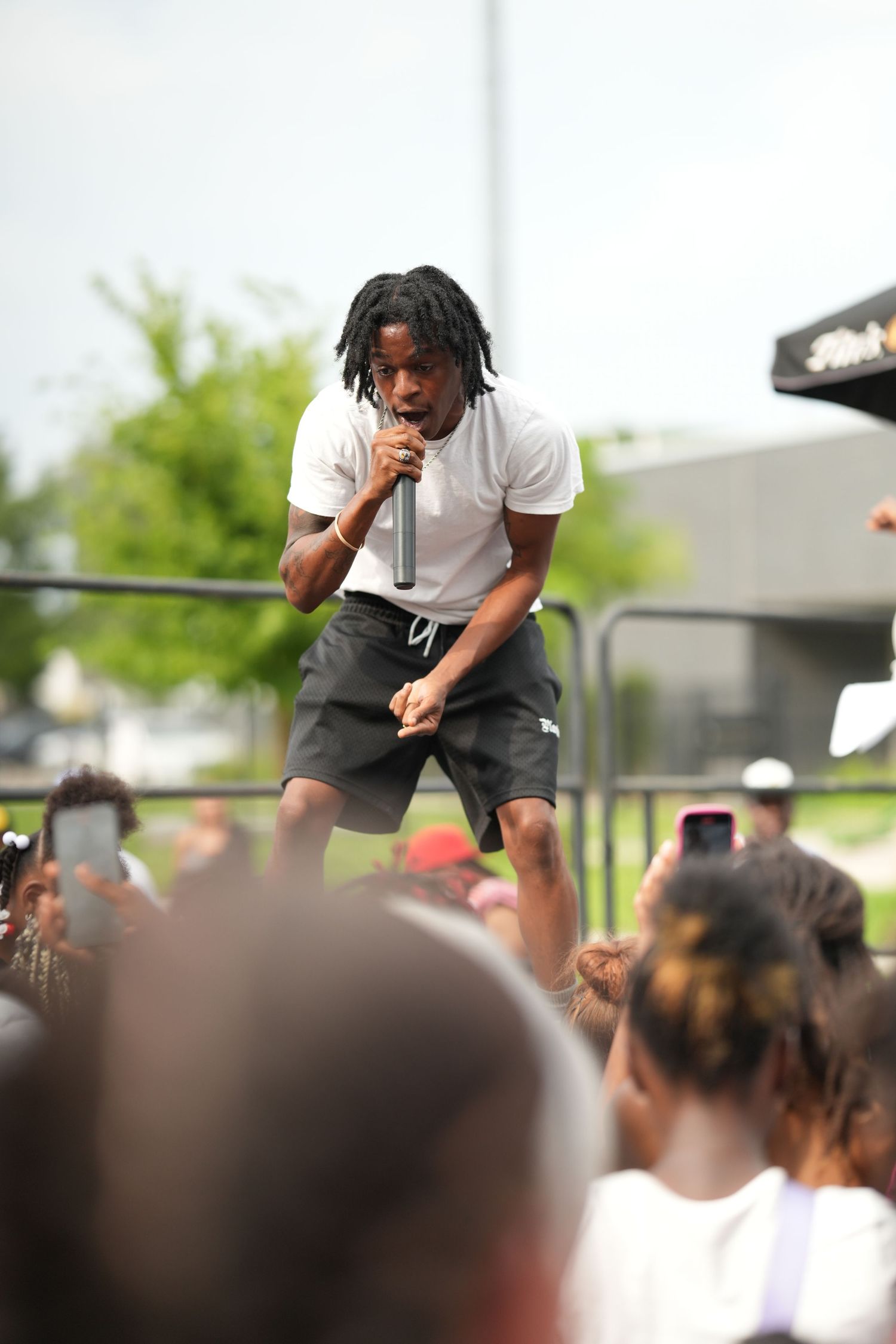 A performer energetically moves on stage in front of a crowd during an outdoor daytime event.