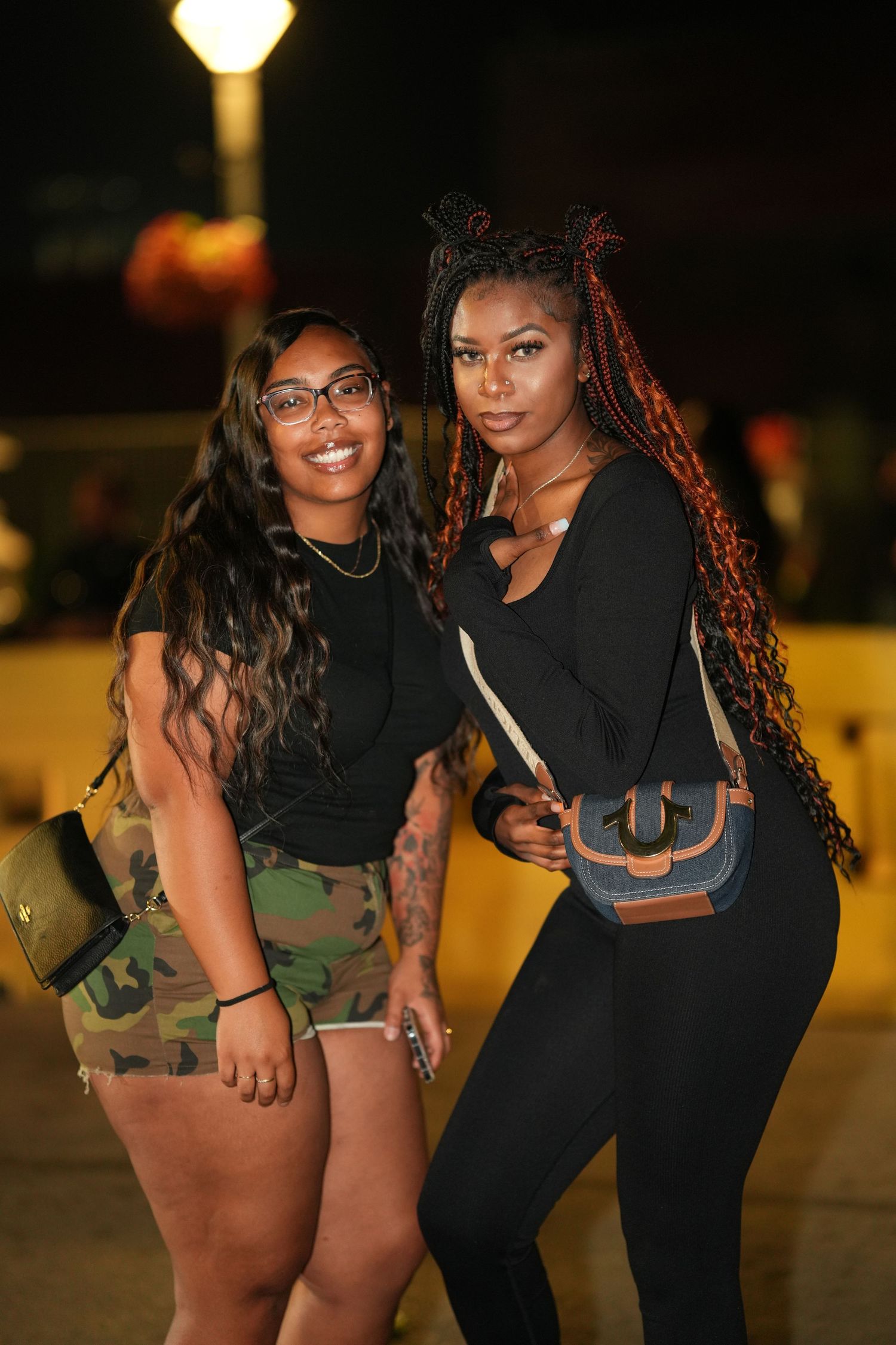 Two friends pose together at night in casual outfits with one wearing camo shorts and another in all black.
