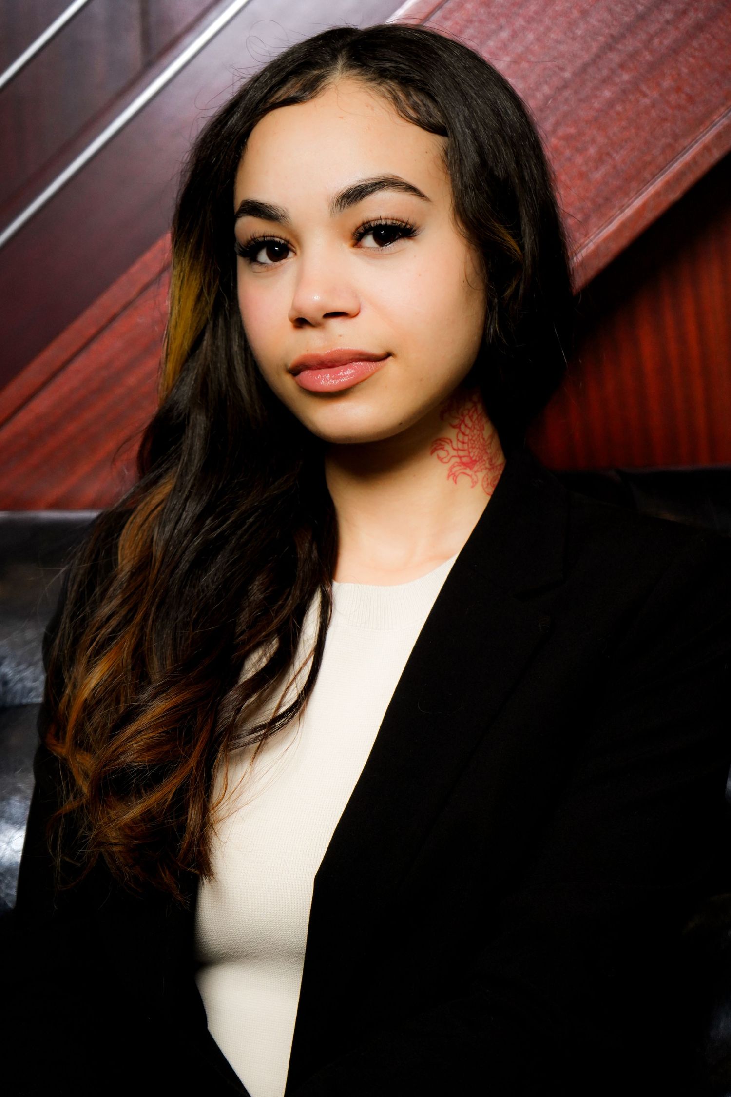 Professional portrait of person in red blazer with braided hair against window background.