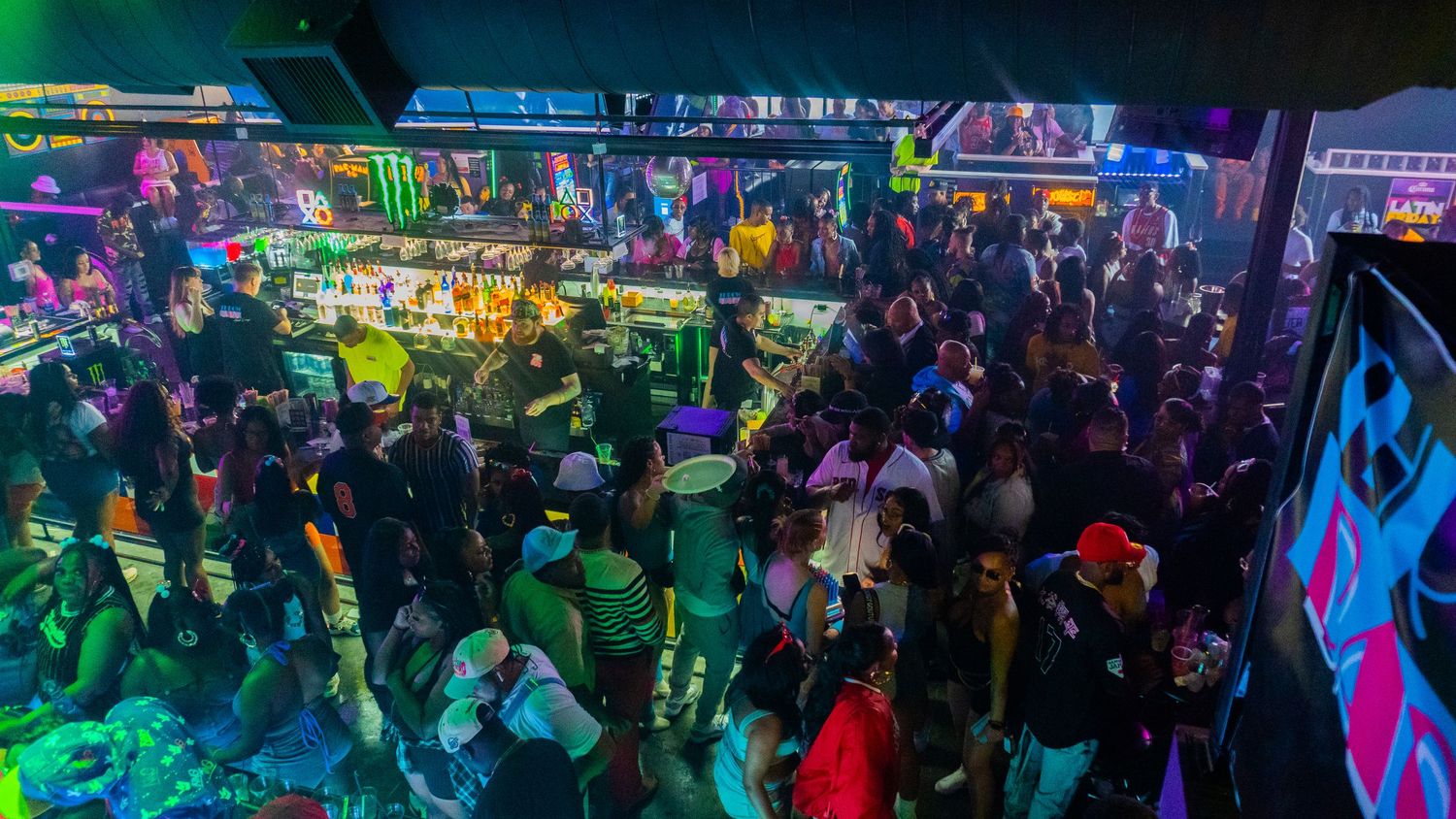 A panoramic view of a crowded nightclub or event space illuminated with colorful neon lights and lasers.