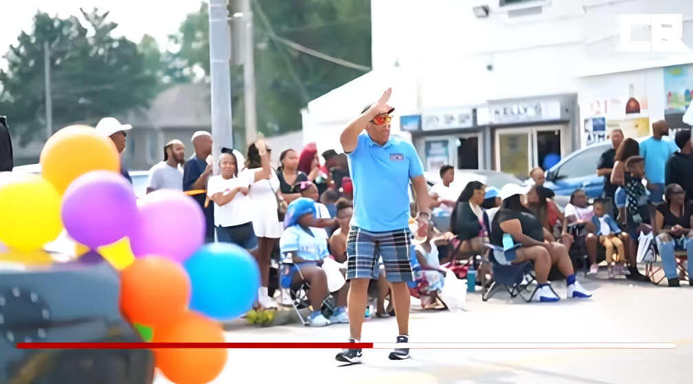 Colorful balloons decorate an outdoor community event with people gathering along a street on a sunny day.