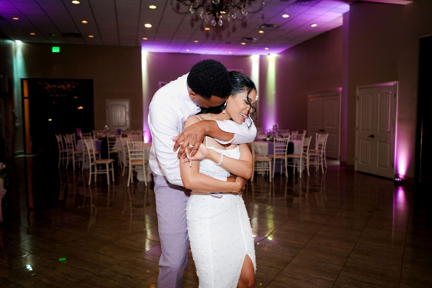 A couple shares a romantic dance in a dimly lit ballroom with purple and green ambient lighting.