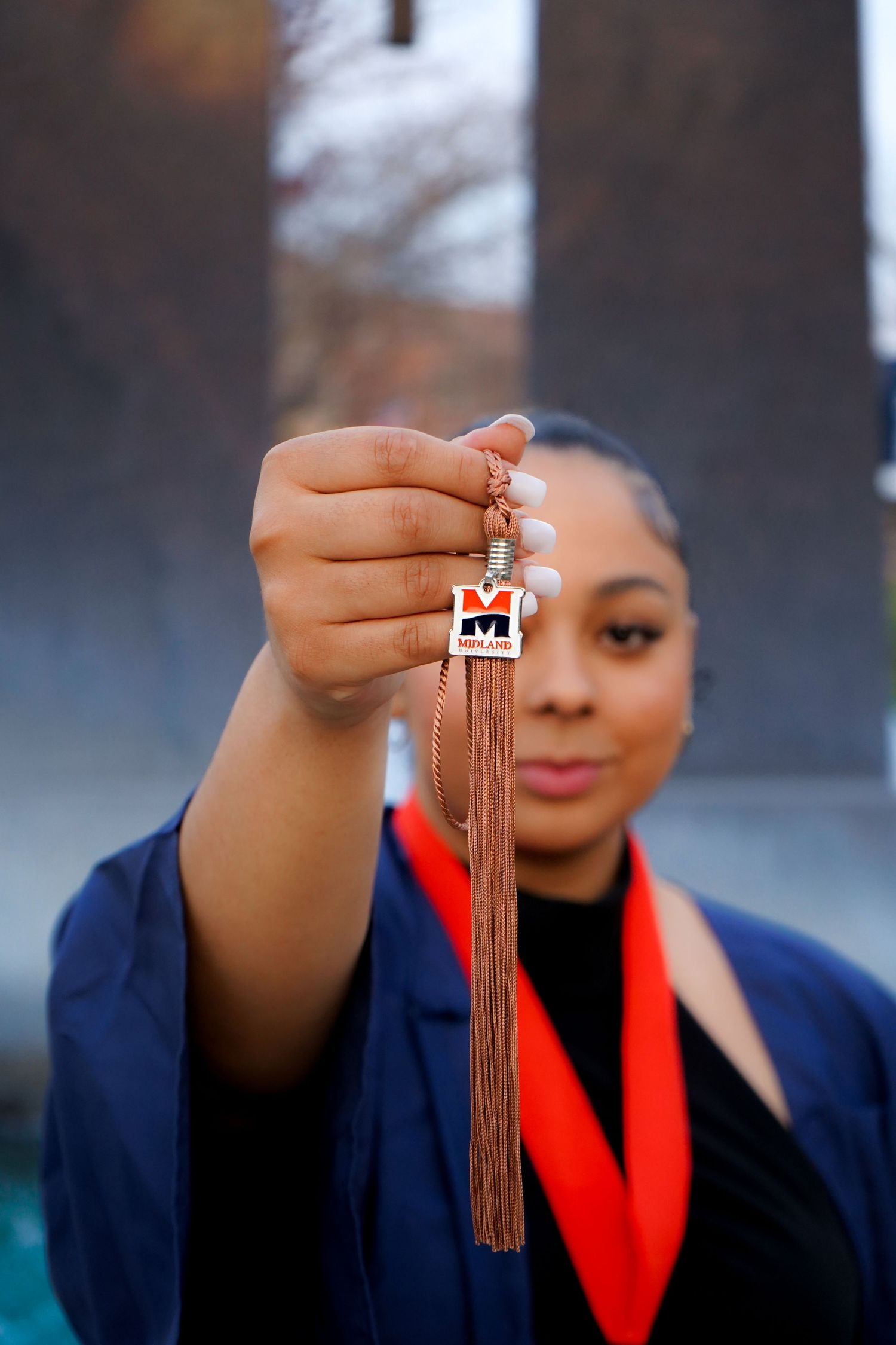 Graduate holding tassel against blurred background in graduation attire.