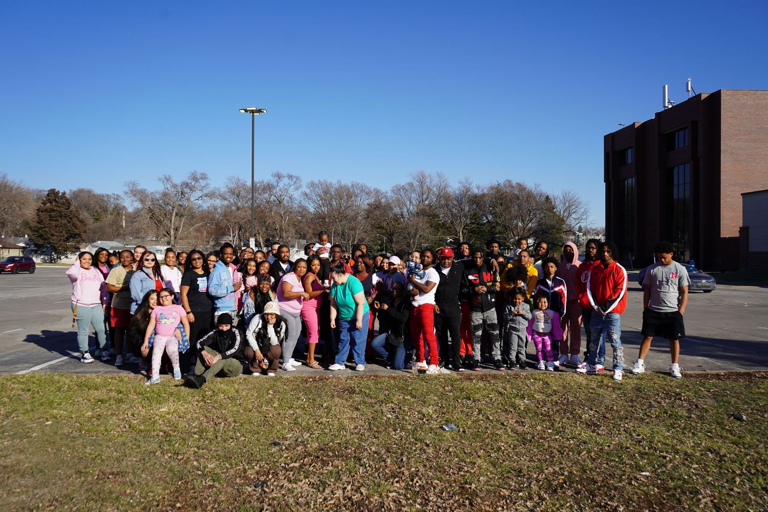 Large group of people gathered outside a building for a community photo on a sunny day.
