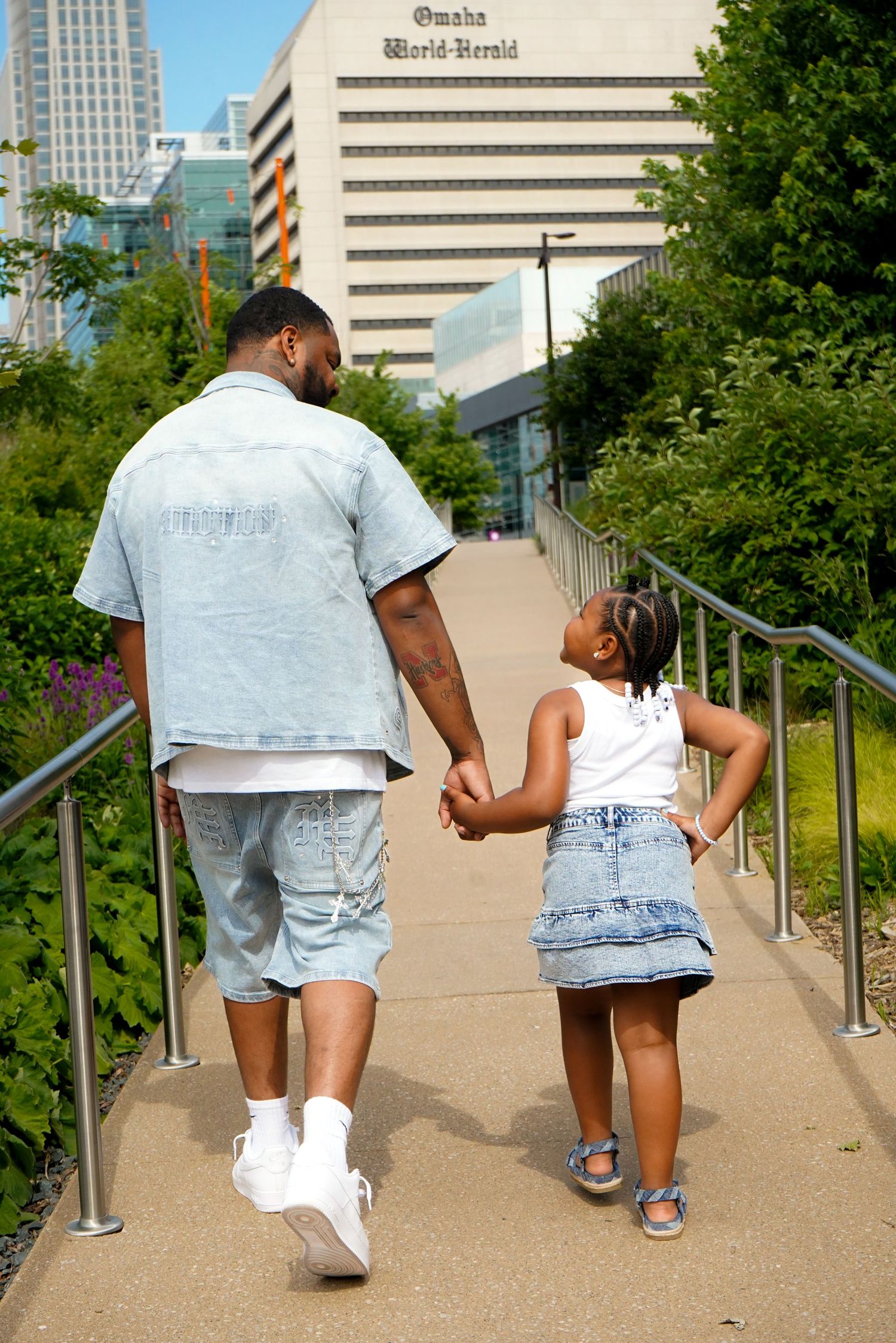 Walking up concrete steps together in coordinated denim outfits on sunny day.