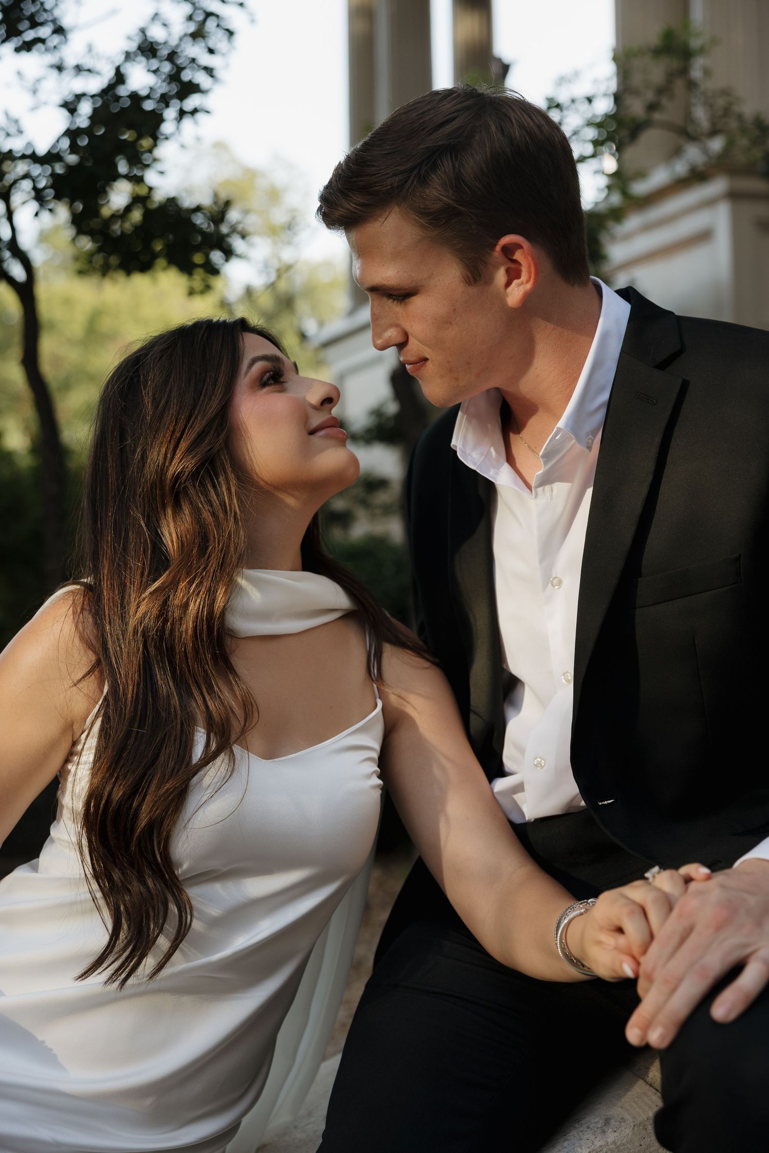 A romantic moment between a couple dressed in white and black formal attire sitting together outdoors.