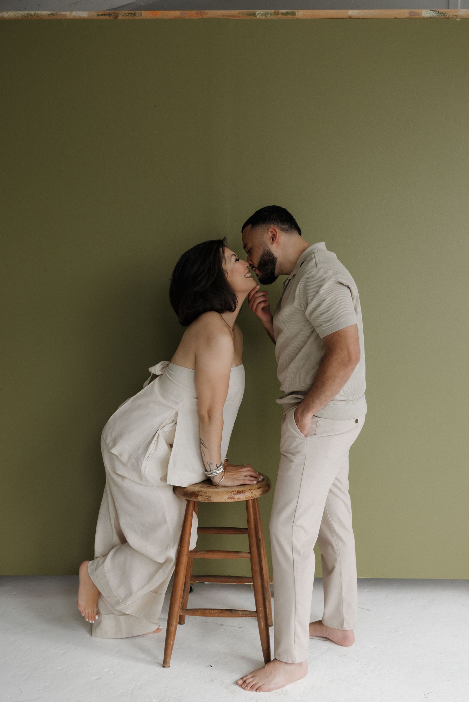 An artistic pregnancy progression photo series showing a couple interacting near a wooden stool against a green wall.