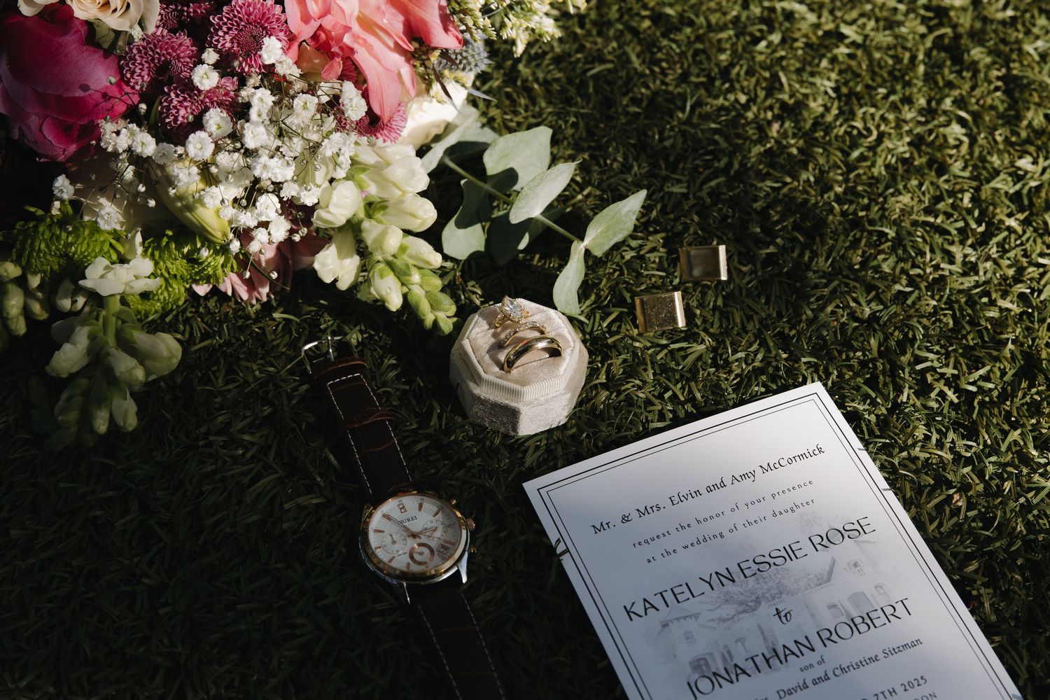 Wedding invitation cards and floral arrangements displayed on grass with pink and white flowers in the background.