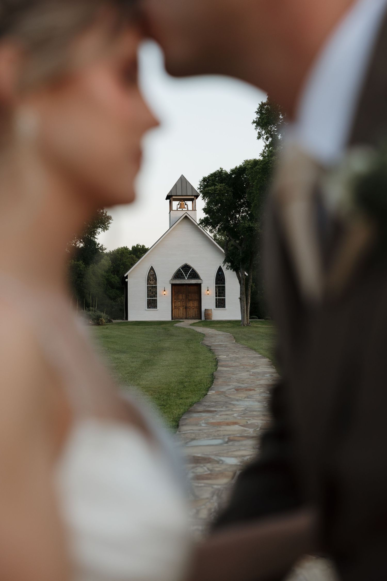 White chapel with steeple framed between blurred couple in foreground.