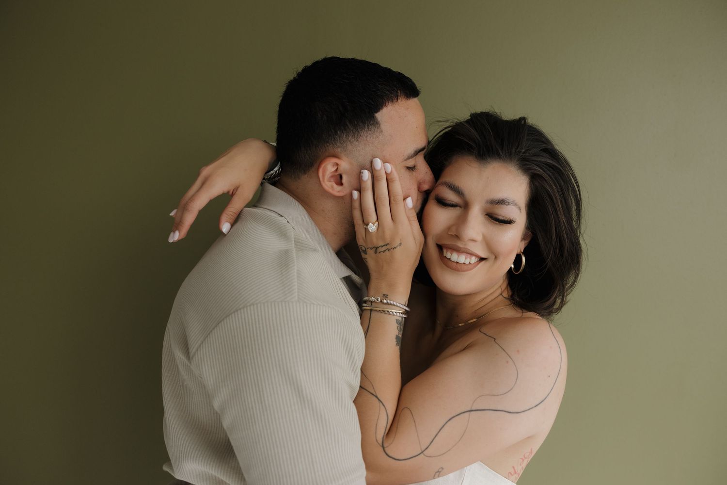 Tender embrace captured against olive green backdrop in studio setting.