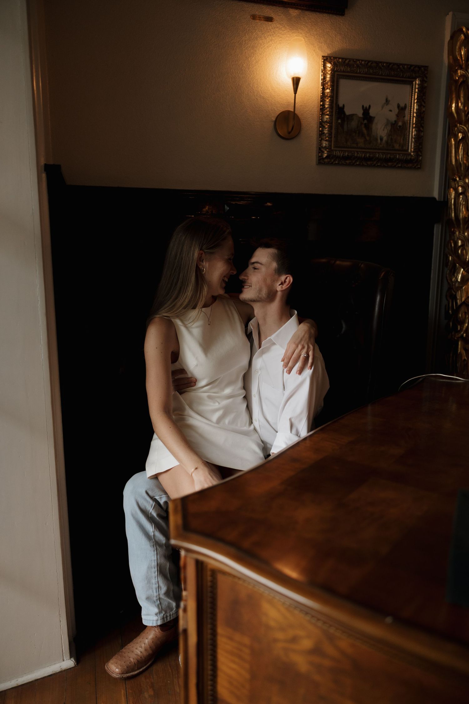 An intimate moment shared between a couple in casual attire sitting on a wooden table in moody indoor lighting.