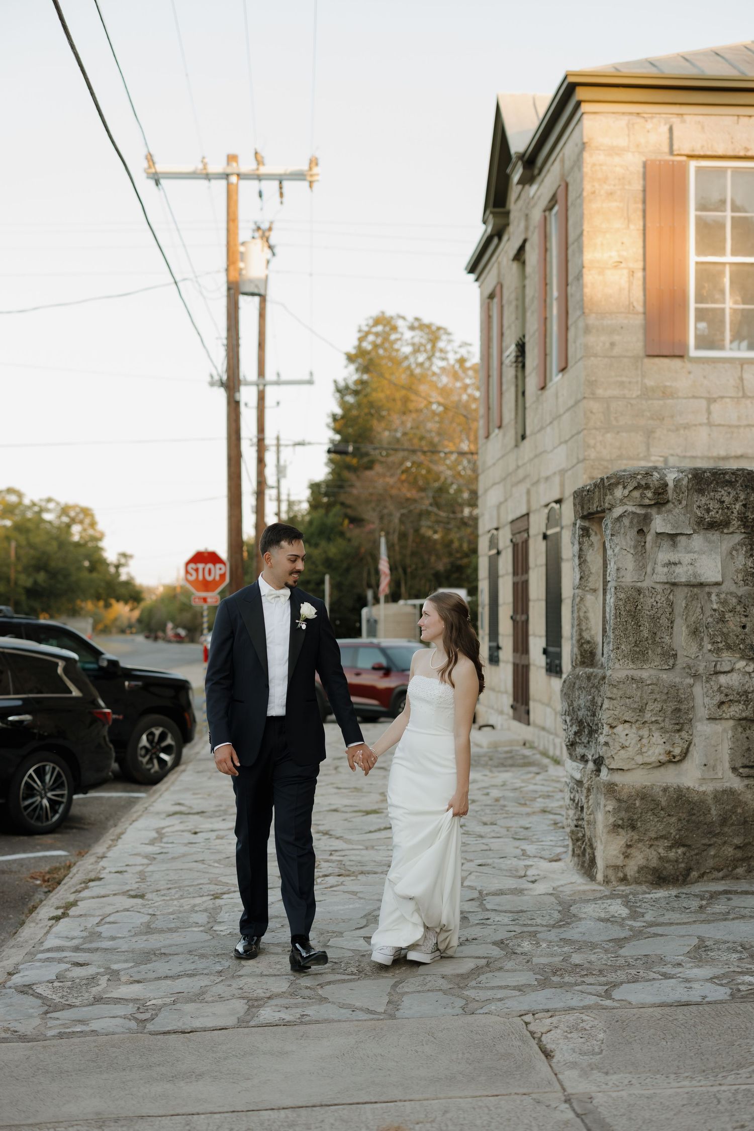 A couple walks along a charming cobblestone street at sunset with historic stone buildings in the background.