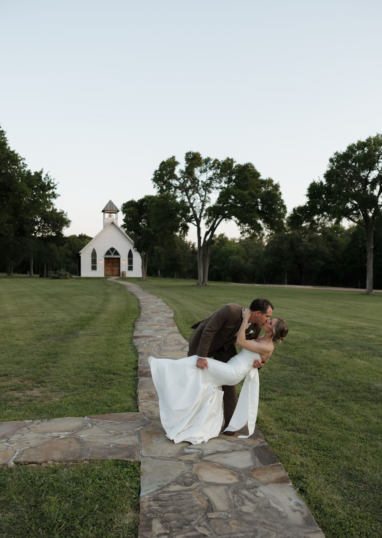 Romantic dip pose on stone path leading to white chapel at dusk.