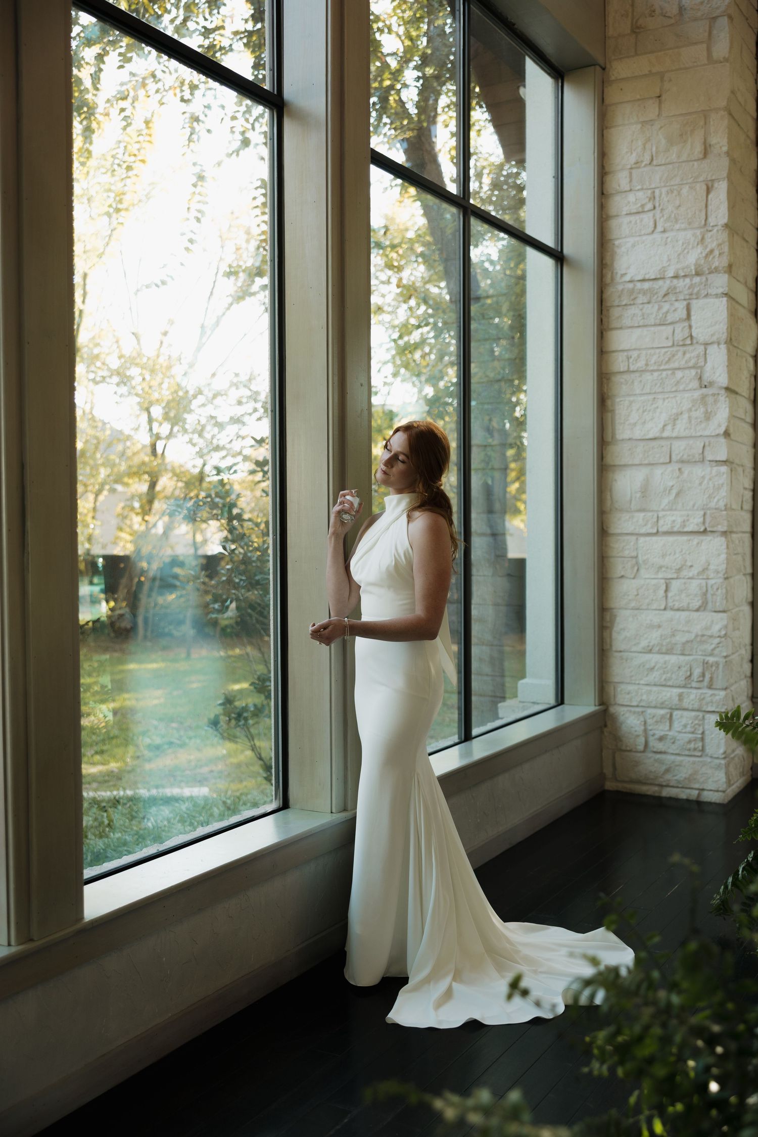 An elegant white wedding gown with a fitted silhouette and train photographed against large windows in natural light.