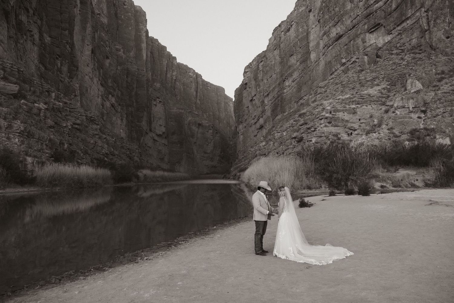 Wedding couple standing by a scenic canyon river surrounded by towering cliffs.