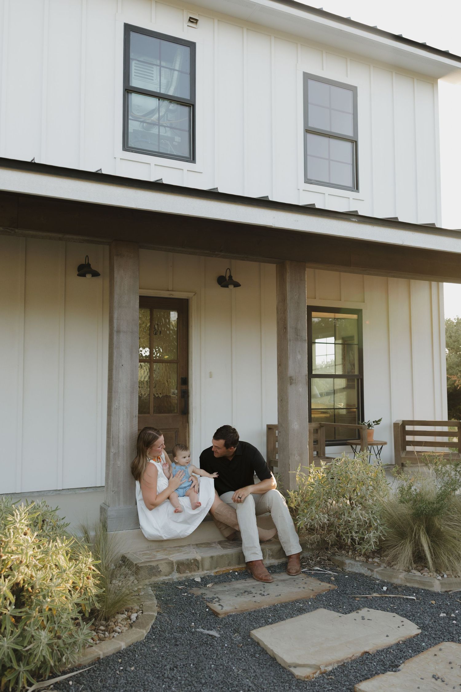 Family sitting together on the front porch steps of a modern farmhouse.