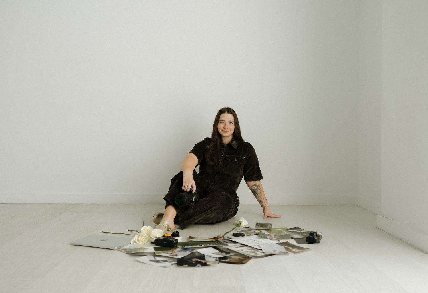 Person in black dress sitting on floor surrounded by scattered documents and photos in minimal white room.
