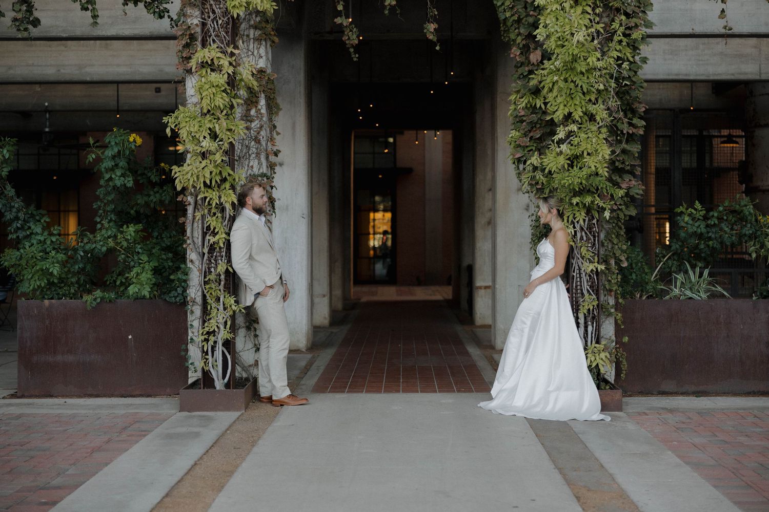 Elegant wedding couple stands apart in a lush vine-covered entryway of an upscale venue at twilight.